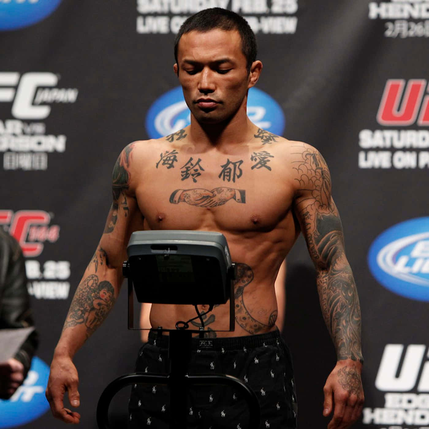 UFC 桌布 壁紙 — 一位有刺青的UFC拳手在品牌背景的稱重活動中赤膊站在體重計上。