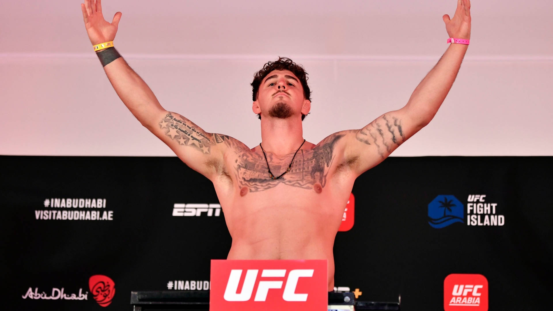 UFC 桌布 壁紙 — 一位有刺青的UFC拳手在阿布達比的稱重活動中勝利地高舉雙臂在磅秤上。