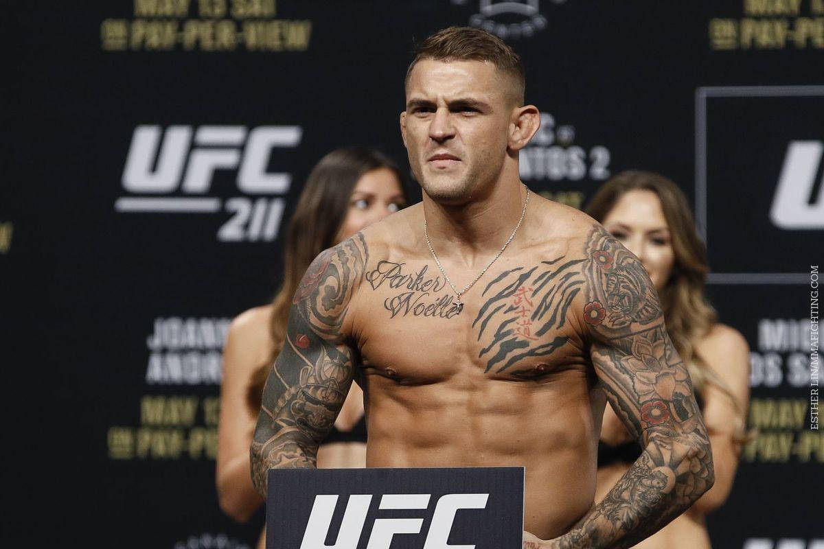 UFC 桌布 壁紙 — 一位有刺青的UFC拳手赤裸上身站在稱重台上，在品牌背景前展現強烈專注力。