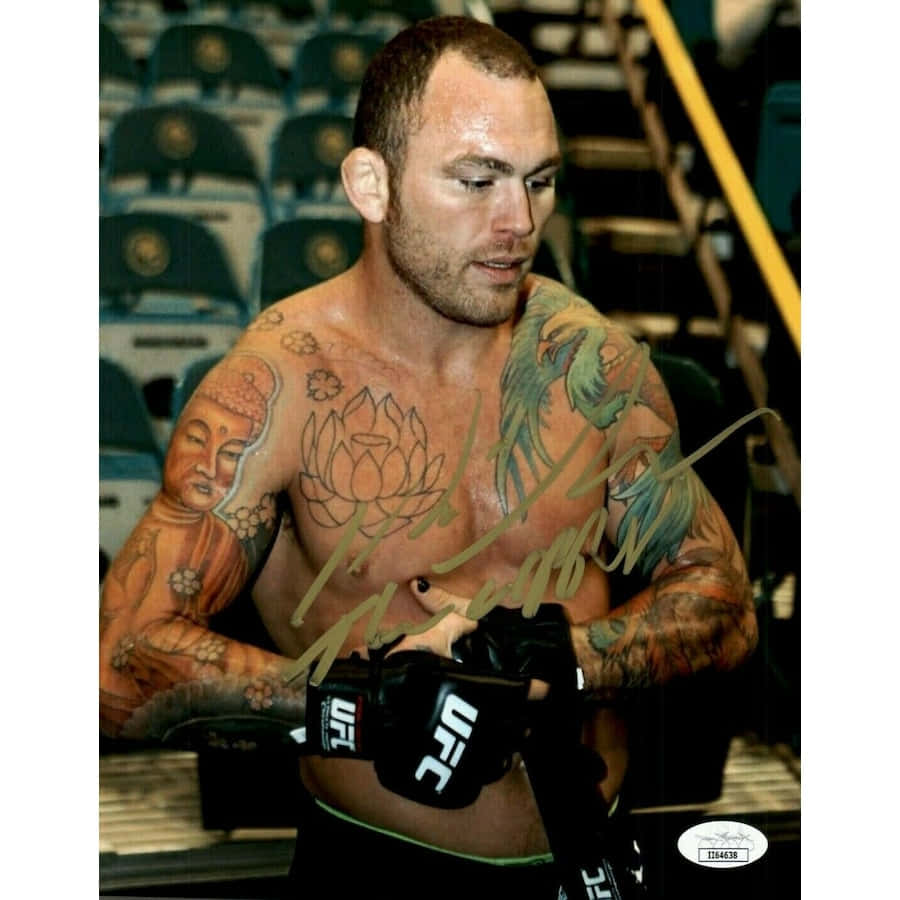 MMA 桌布 壁紙 — 一位有刺青的UFC拳擊手戴著黑色手套站在一個後面有藍色空座位的場館中。