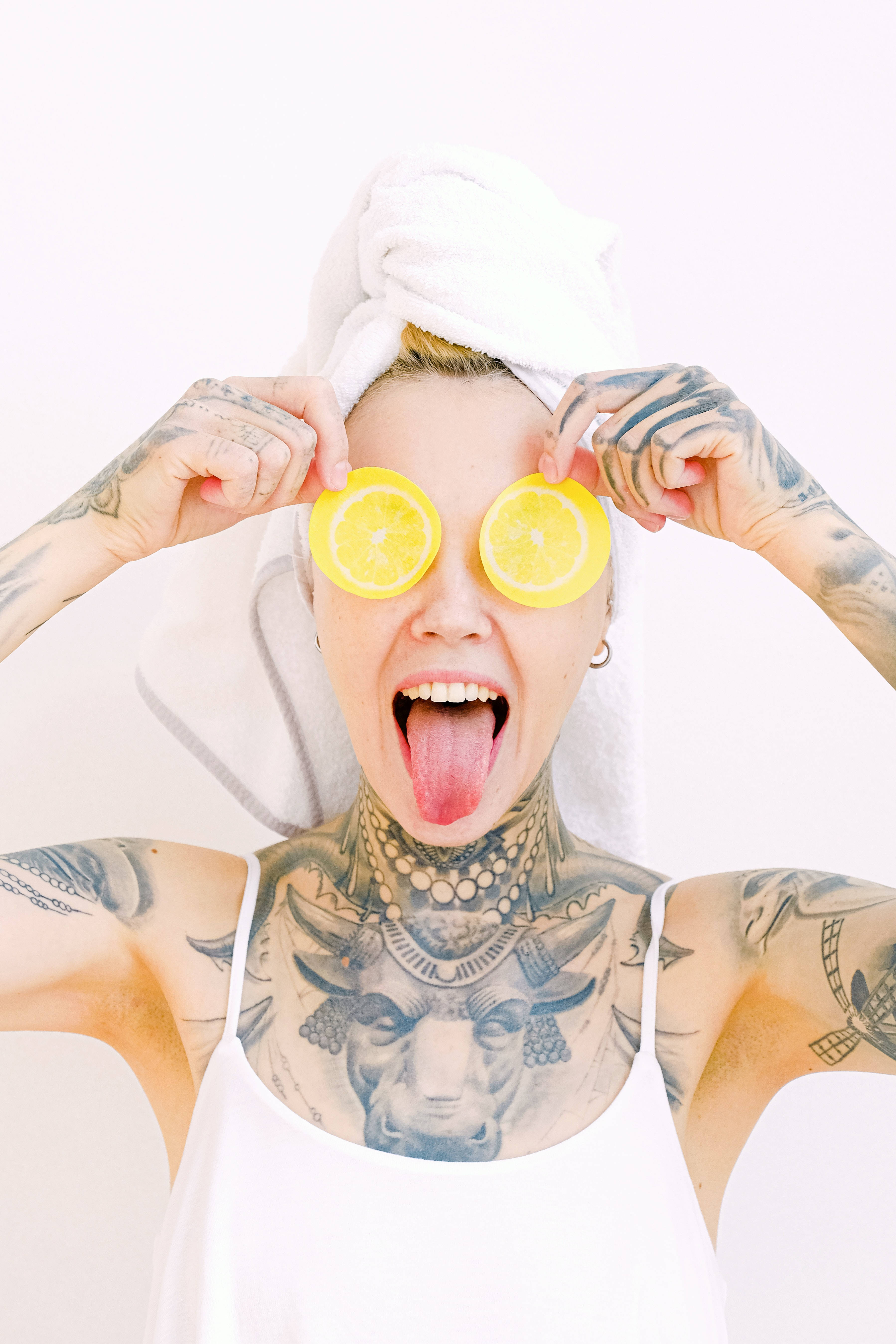 Tattoo 桌布 壁紙 — 一位有刺青的女性，頭上裹著毛巾，頑皮地將檸檬片放在眼睛上，同時伸出舌頭。