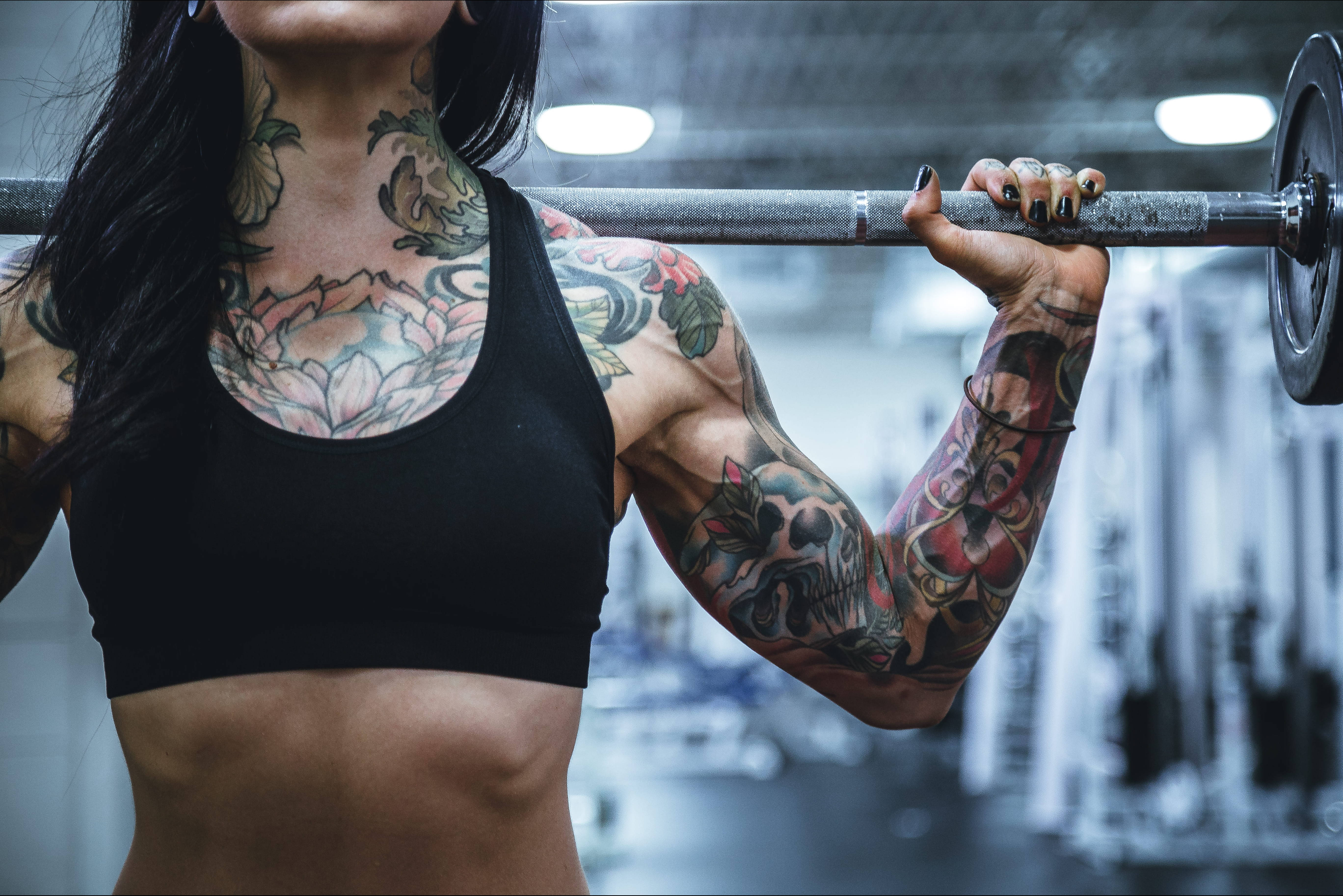 Barbell 桌布 壁紙 — 一位有刺青的女性在健身房專注地舉起槓鈴，肌肉線條分明。
