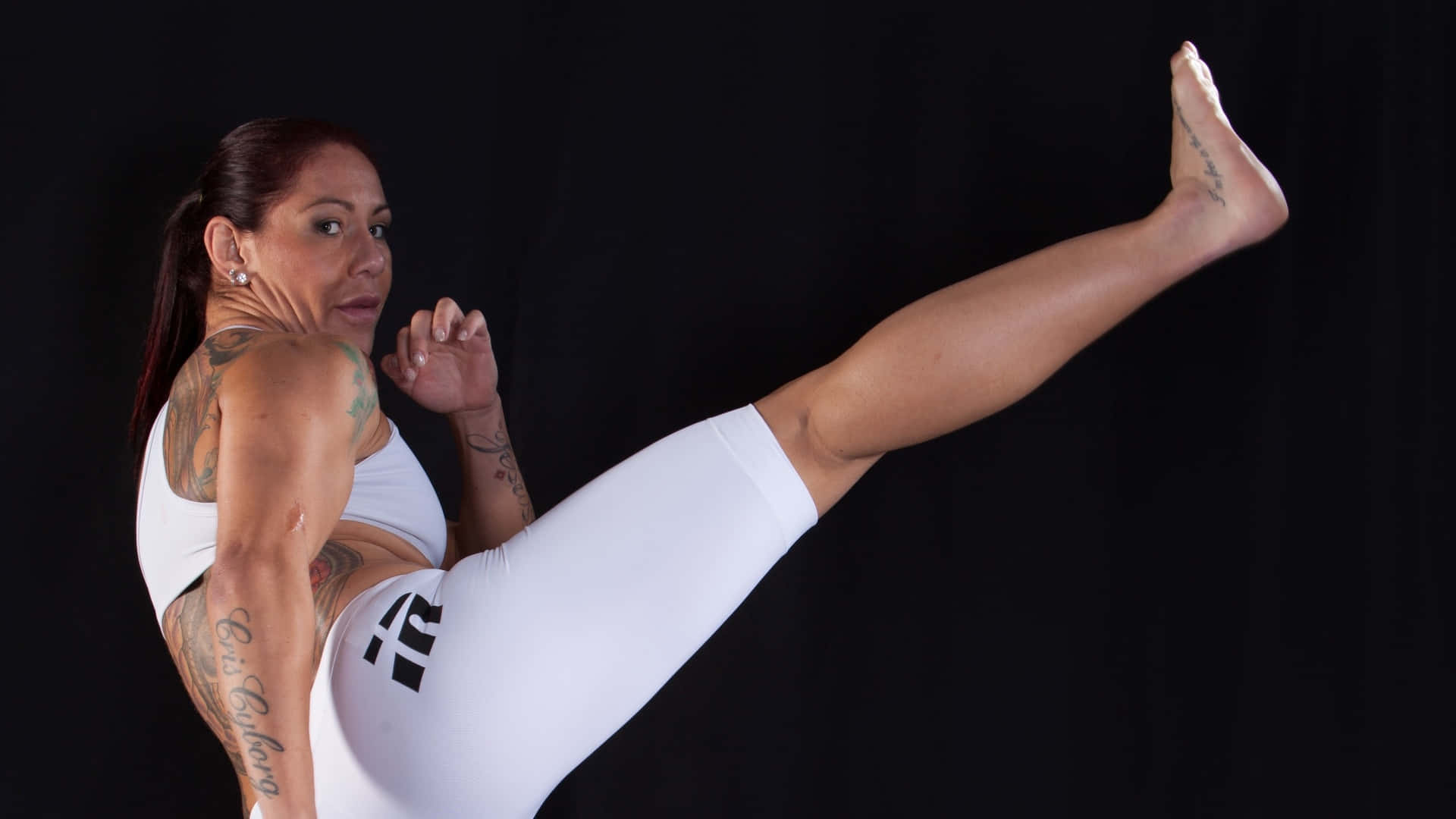 MMA 桌布 壁紙 — 一位有刺青的女性穿著白色運動服，在黑色背景下執行高踢腿動作。