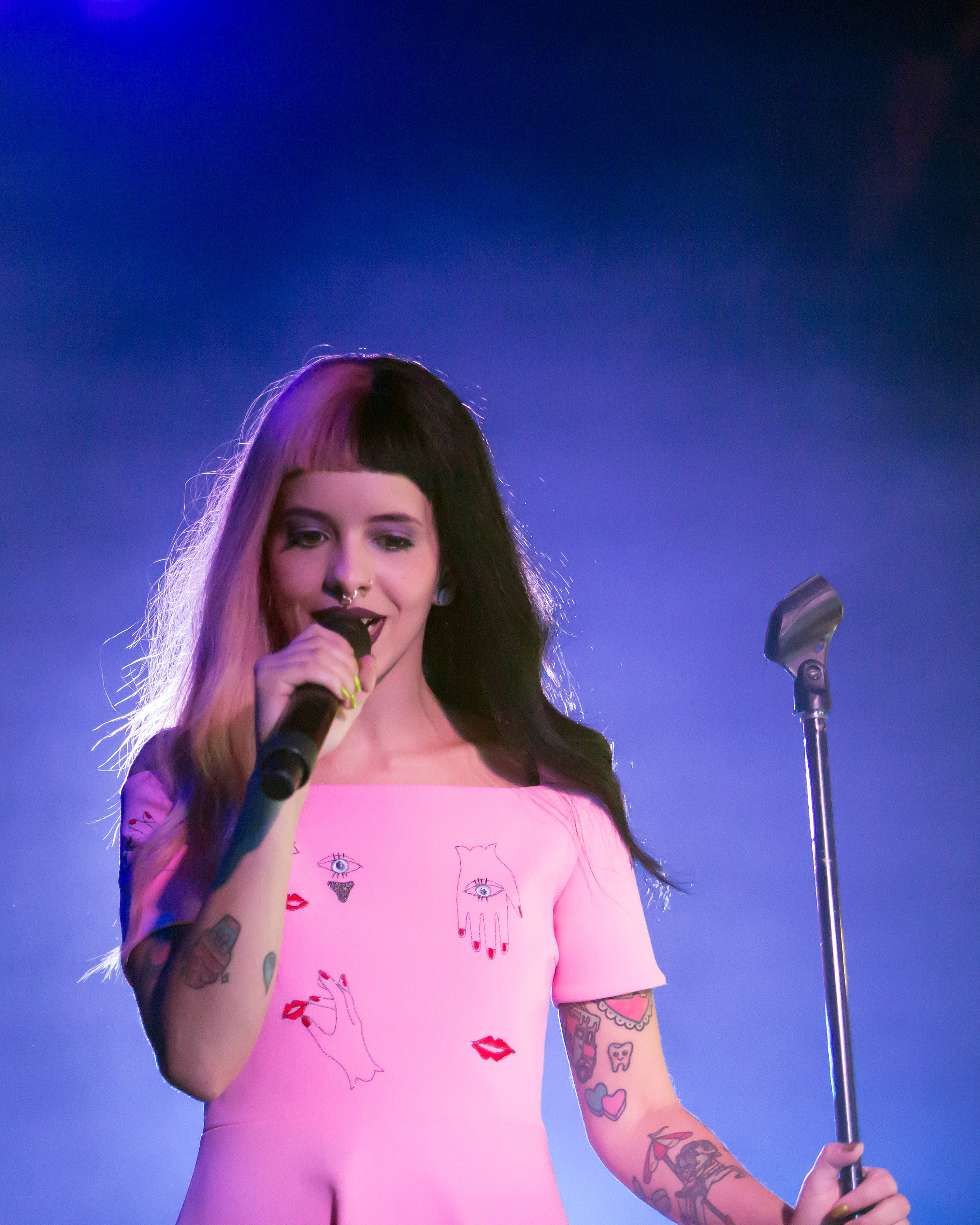 Melanie 桌布 壁紙 — 一位有刺青的女歌手穿著粉紅色服裝，在藍色舞台燈光下拿著麥克風表演。