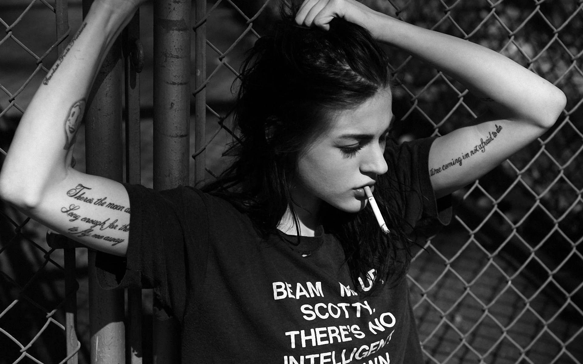 bad 桌布 壁紙 — 一位有刺青的年輕女子靠在鐵絲網圍欄上抽煙，黑白照片。
