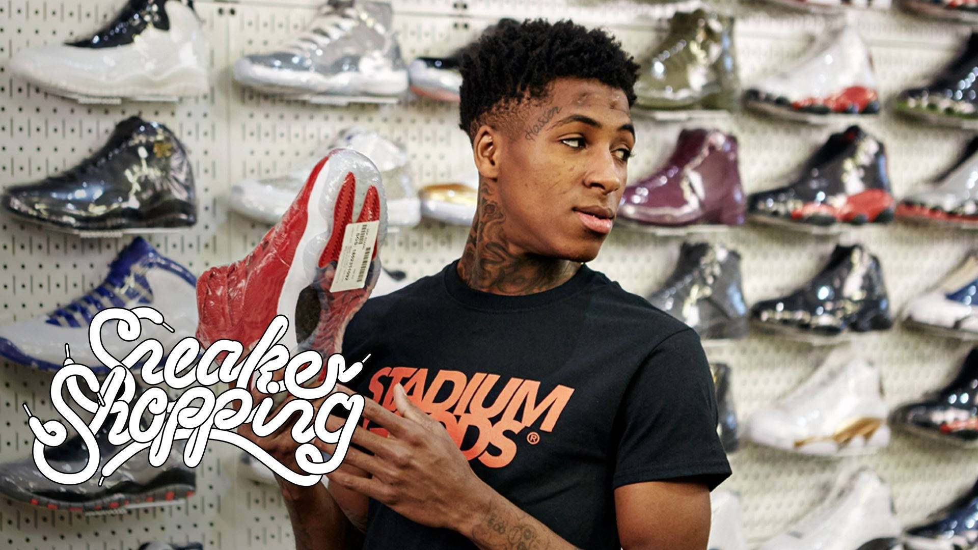 Youngboy 桌布 壁紙 — 一位有刺青的年輕男子在一個掛滿彩色運動鞋的釘板牆商店裡，拿著一雙紅白相間的運動鞋。