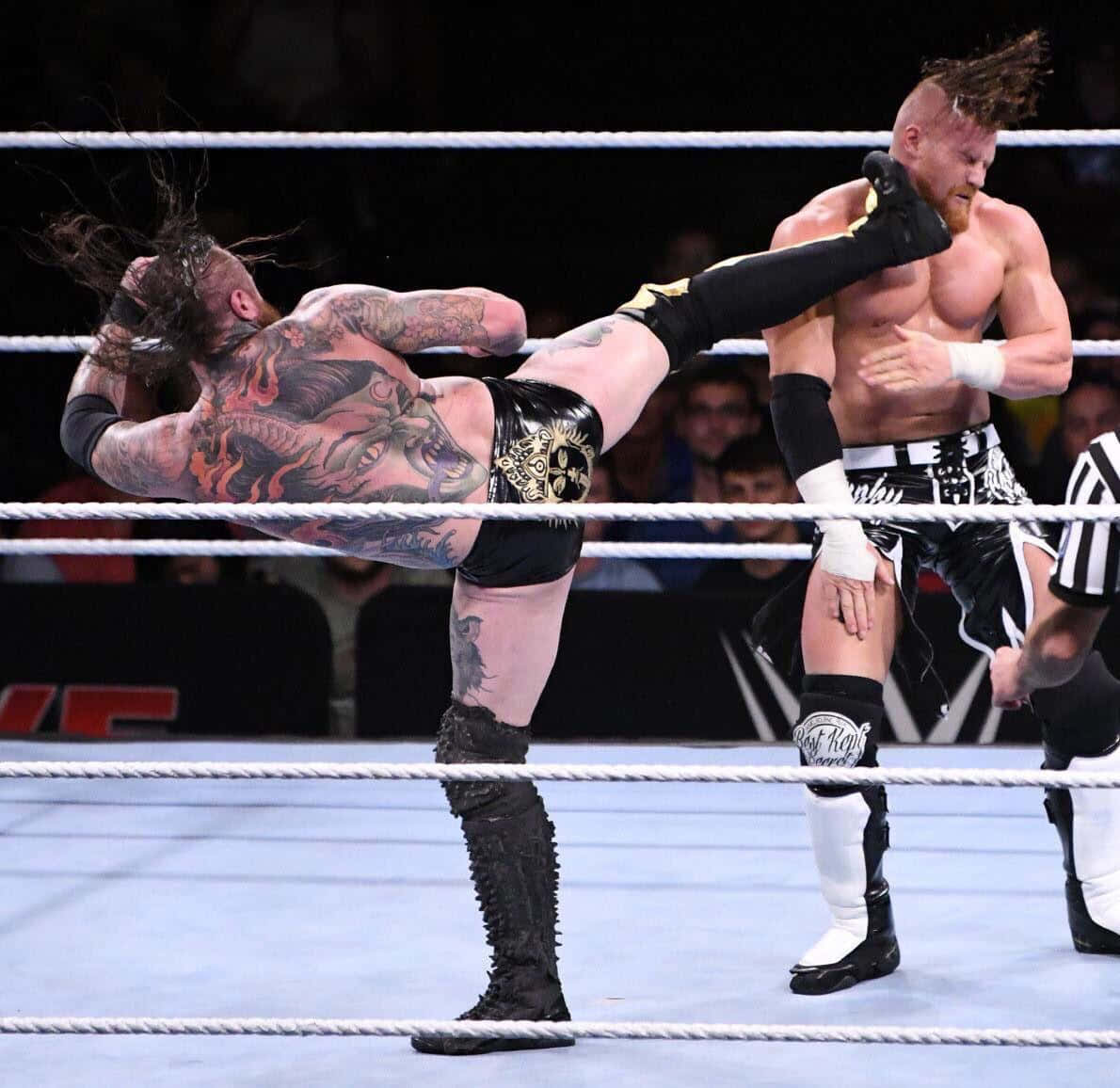 WWE 桌布 壁紙 — 一位有刺青的摔角手在燈光明亮的摔角場內對對手使出高飛踢。