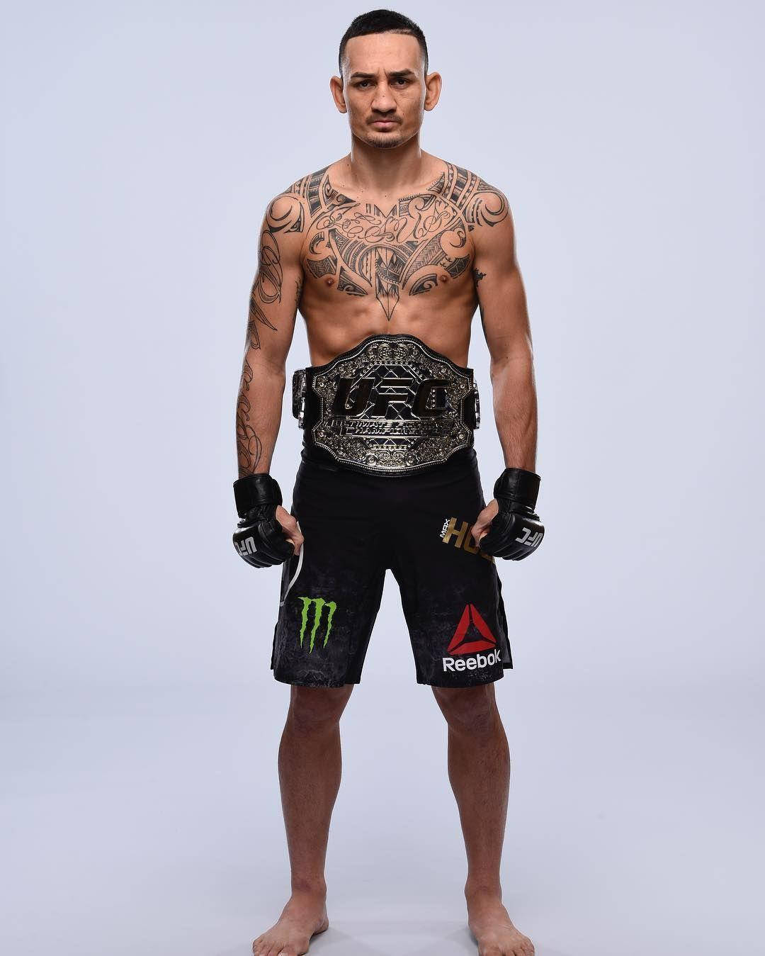 UFC 桌布 壁紙 — 一位有刺青的混合武術家自信地站著，戴著冠軍腰帶和品牌短褲，背景是簡單的攝影棚。