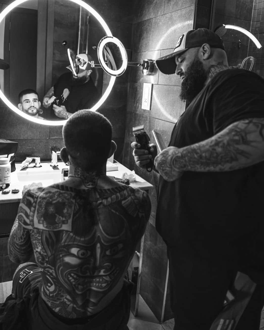 Haircut 桌布 壁紙 — 一位有刺青的理髮師在現代理髮店中為客人修剪頭髮，店內有圓形環形燈和鏡子反射場景。