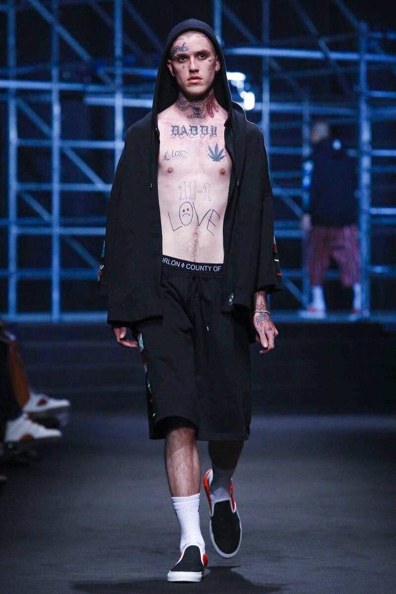 Fashion Model 桌布 壁紙 — 一位有刺青的男模特兒在藍色舞台燈光下穿著黑色連帽衫和短褲走秀。
