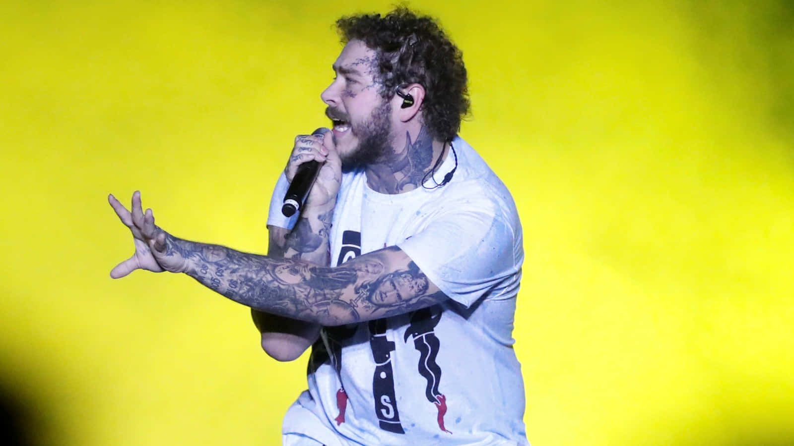 Post Malone 桌布 壁紙 — 一位有刺青的男歌手在充滿活力的黃色背景下於舞台上熱情演出。