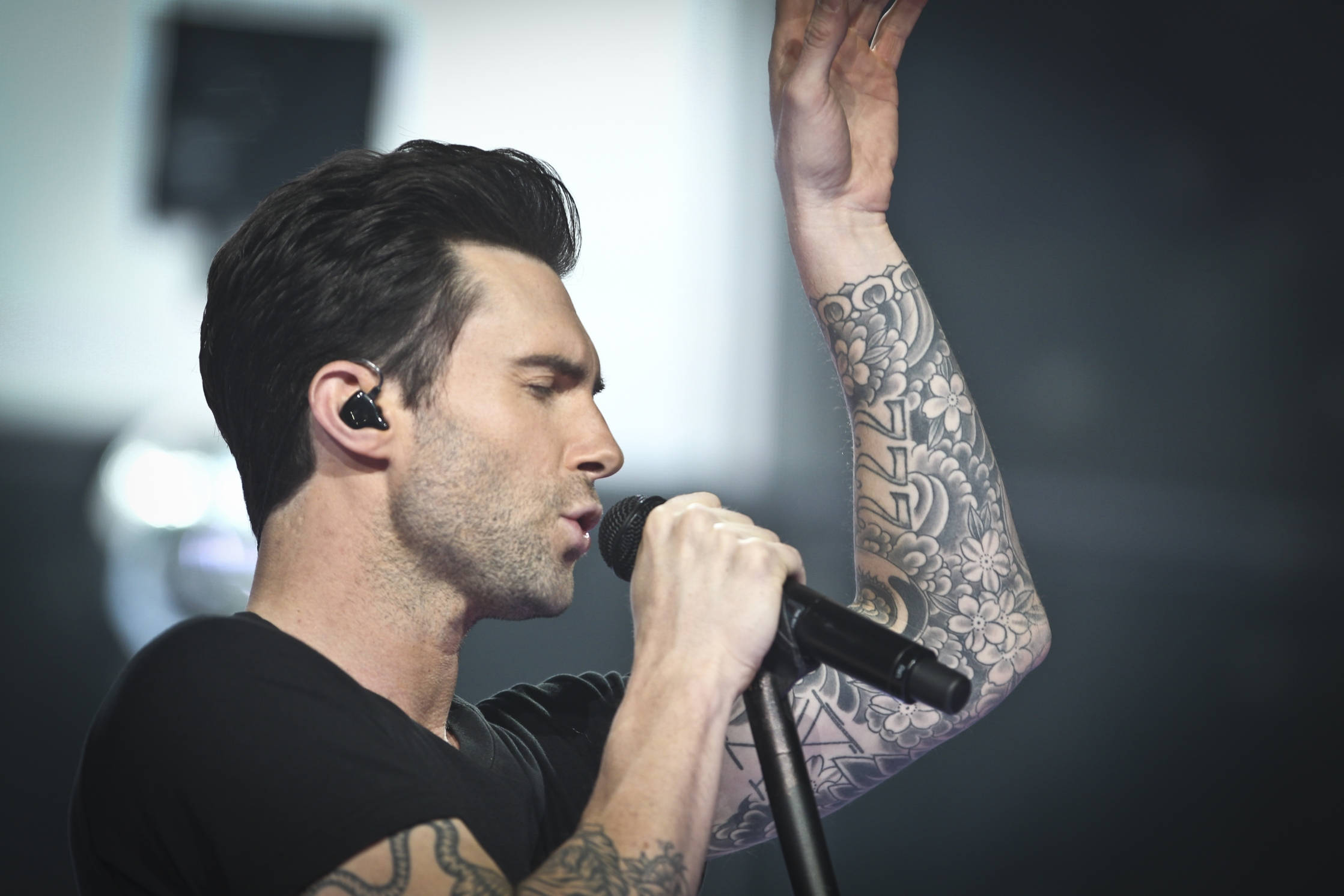 Adam Levine 桌布 壁紙 — 一位有刺青的男歌手在昏暗的舞台上對著麥克風熱情表演。