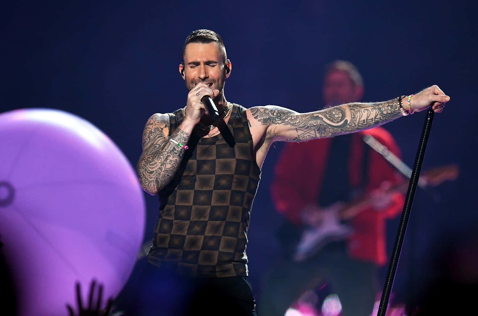 Adam Levine 桌布 壁紙 — 一位有刺青的男歌手在紫色燈光下熱情地表演，手持麥克風和麥克風架。