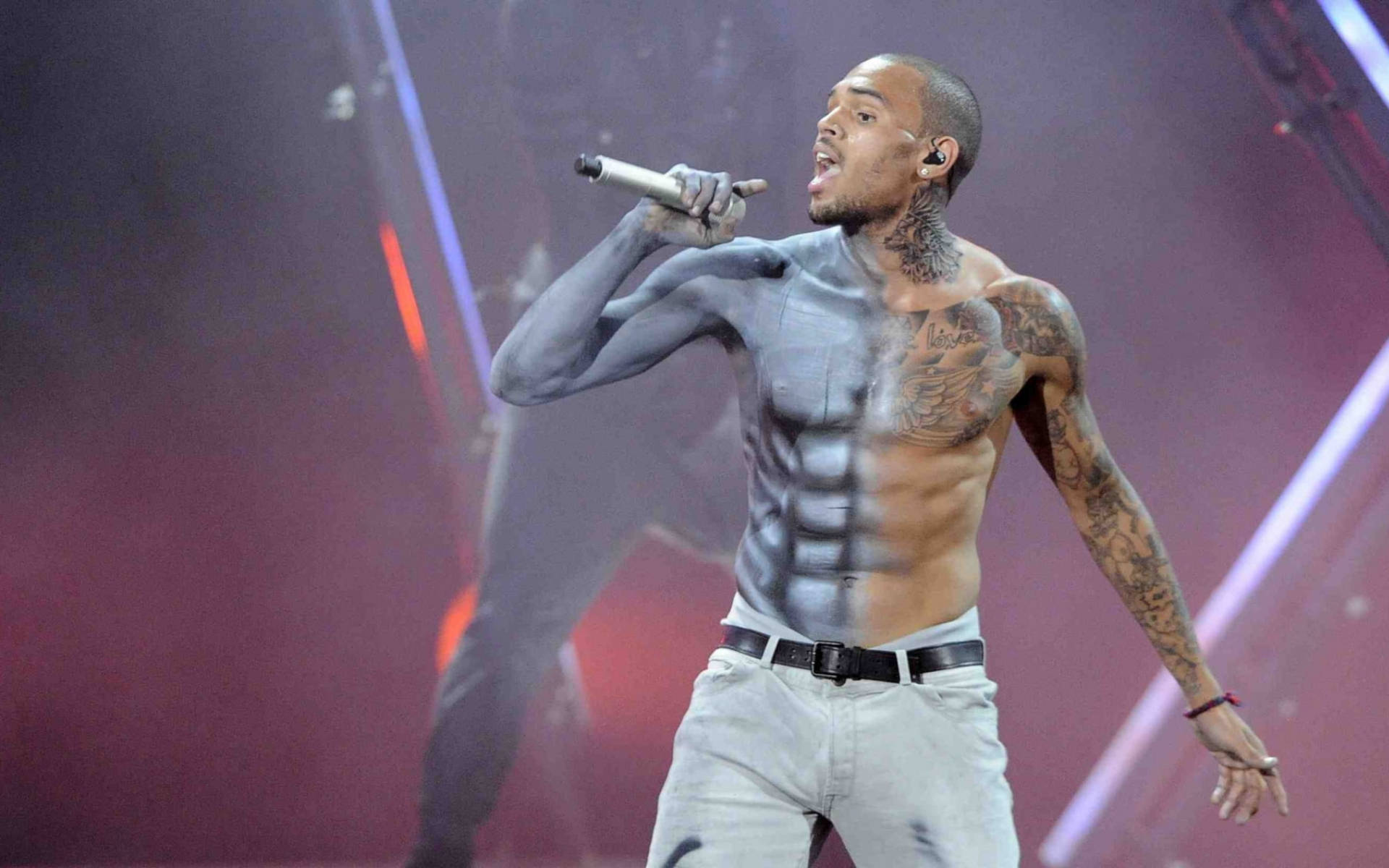 Chris Brown 桌布 壁紙 — 一位有刺青的男歌手在舞台上赤裸上身，在戲劇性的紅色和紫色舞台燈光下拿著麥克風表演。