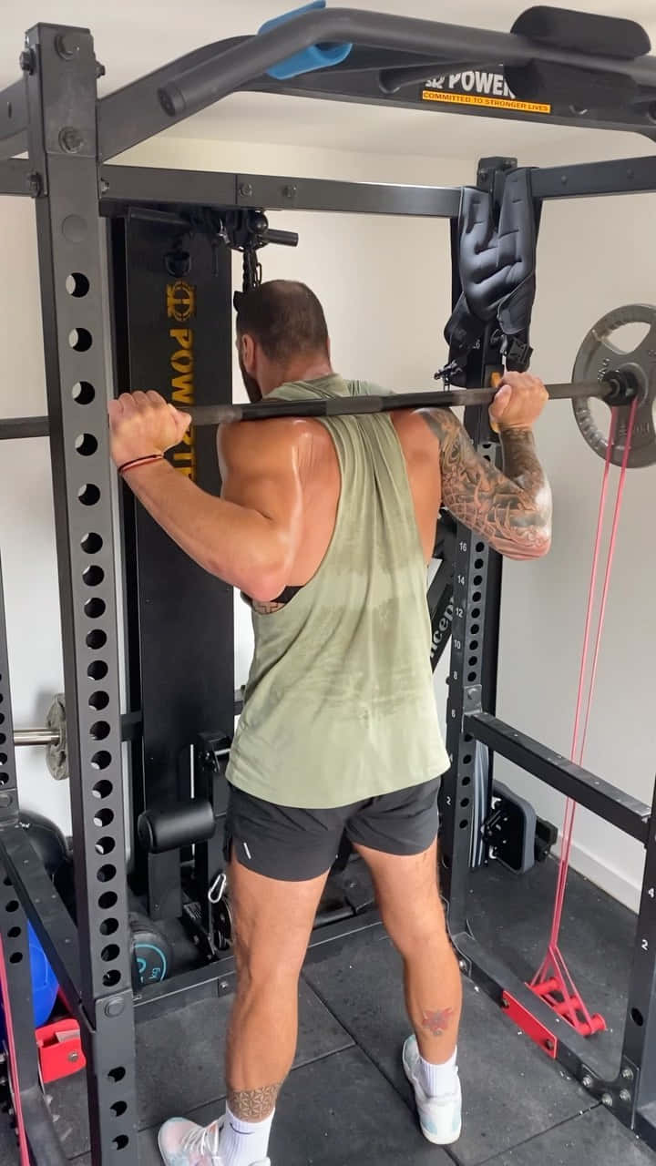 Fitness 桌布 壁紙 — 一位有刺青的肌肉男在家中的健身房，周圍都是舉重器材，正在進行槓鈴划船。