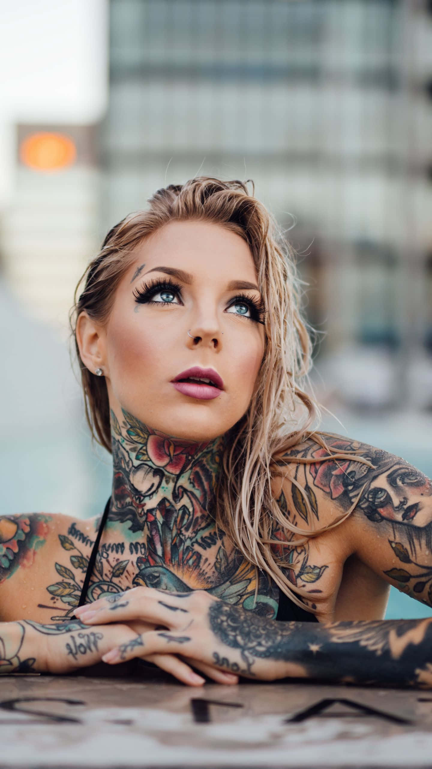 Tattoo 桌布 壁紙 — 一位有刺青的金髮女性在模糊的城市背景下向上凝視。