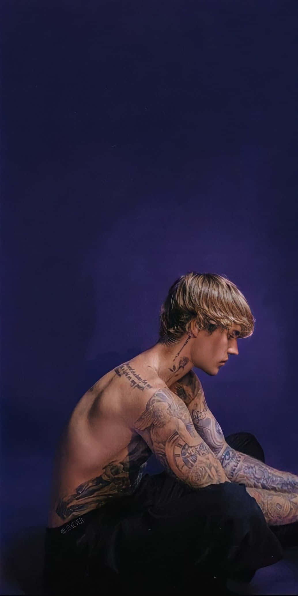 Justin Bieber 2021 桌布 壁紙 — 一位有刺青的金髮男子側面坐在深紫色背景前，目光向下。