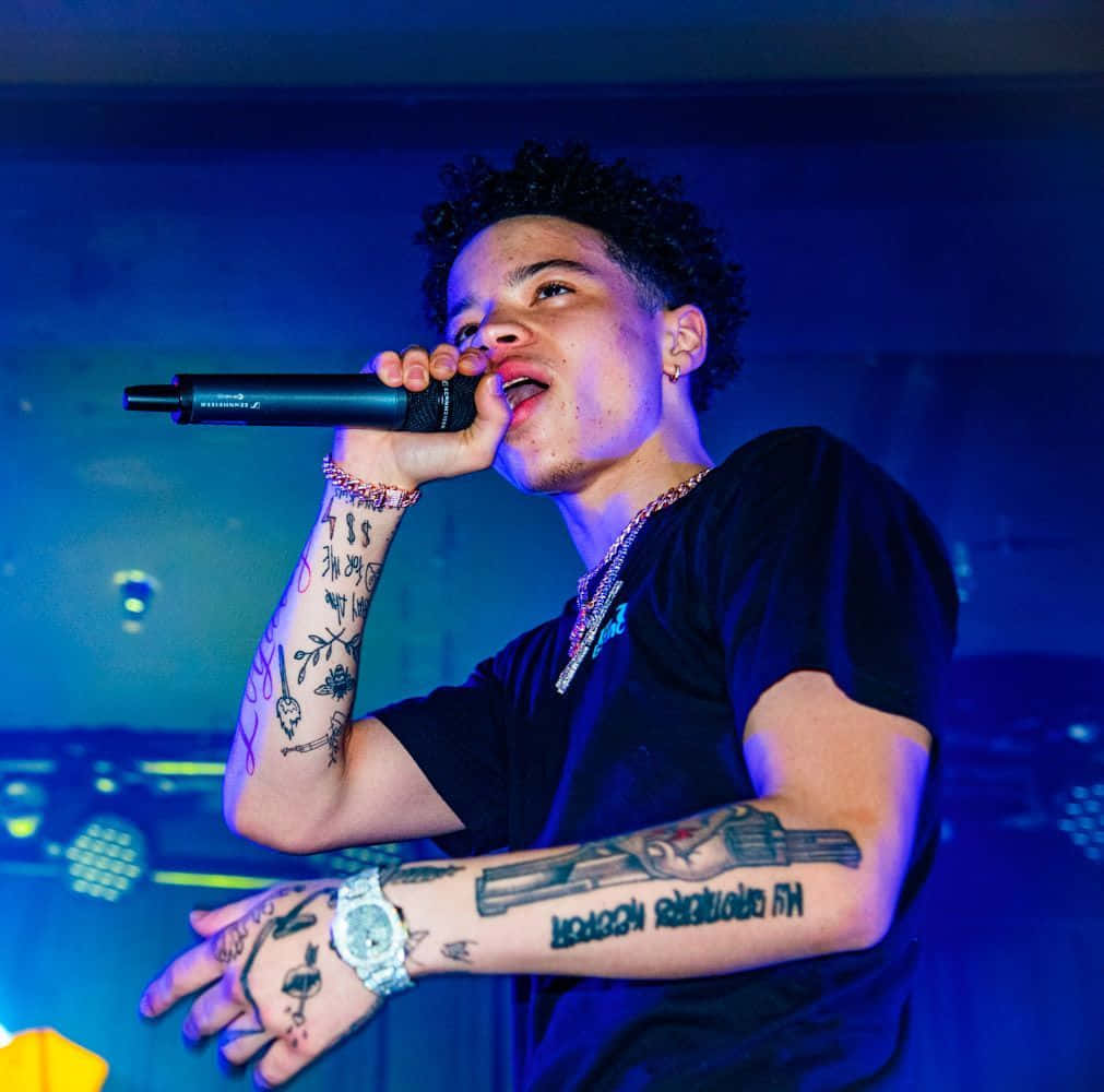 Lil Mosey 桌布 壁紙 — 一位有刺青的饒舌歌手在強烈的藍色舞台燈光下，對著麥克風熱情表演。