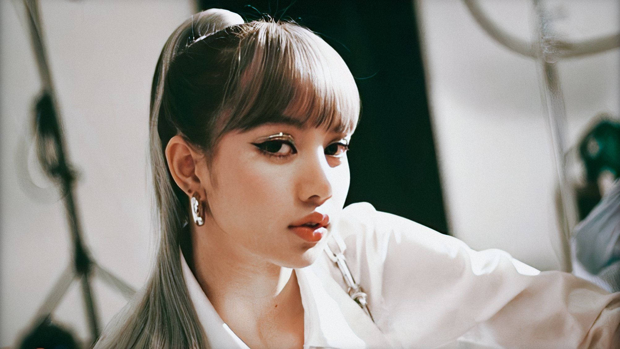 Lalisa 桌布 壁紙 — 一位有瀏海和高馬尾的年輕女性在柔和光線的攝影棚中若有所思地凝視，可見設備。