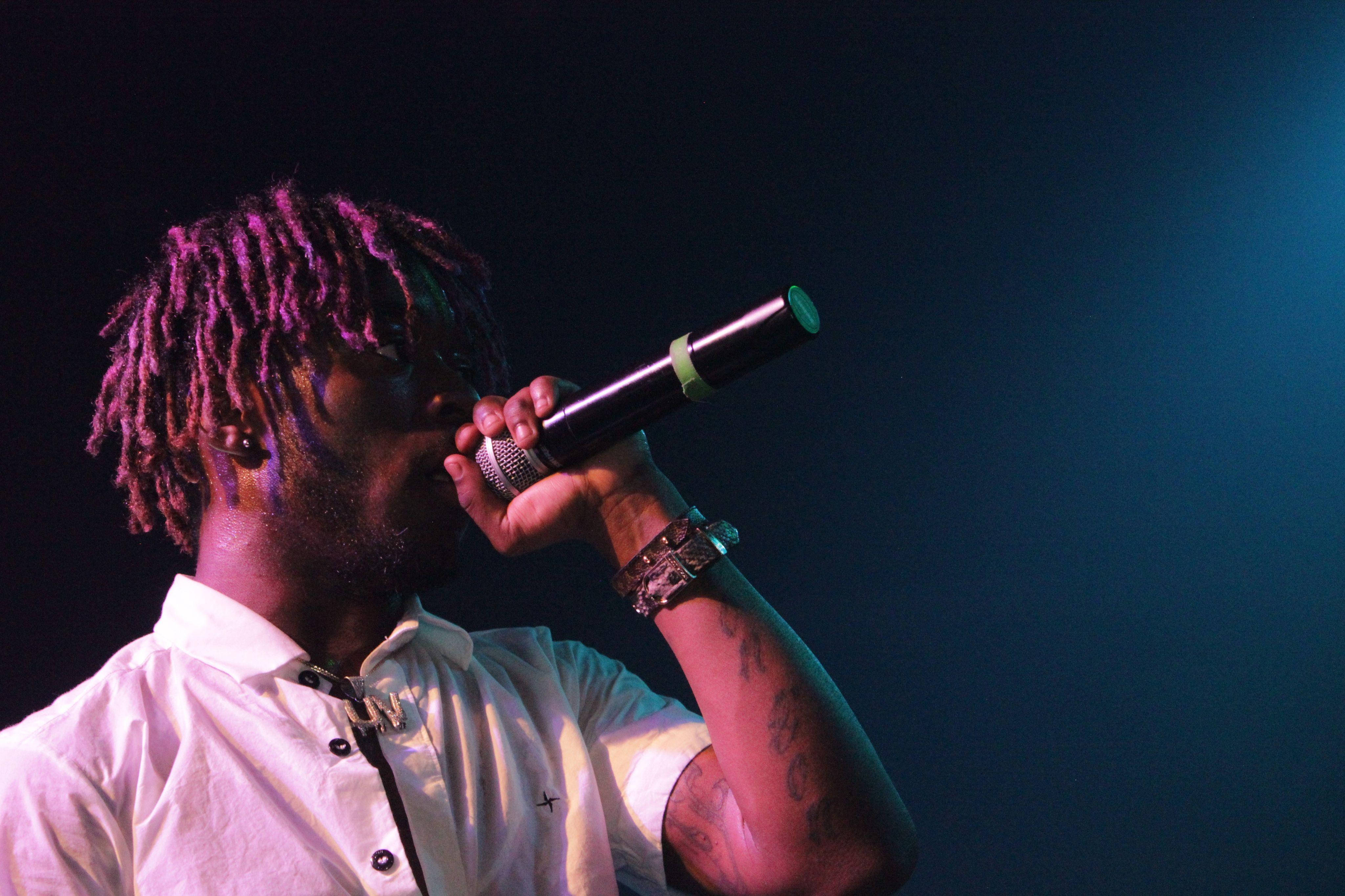Lil Uzi Desktop 桌布 壁紙 — 一位染有紫色辮子頭的音樂家在戲劇性的藍色舞台燈光下對著麥克風唱歌。