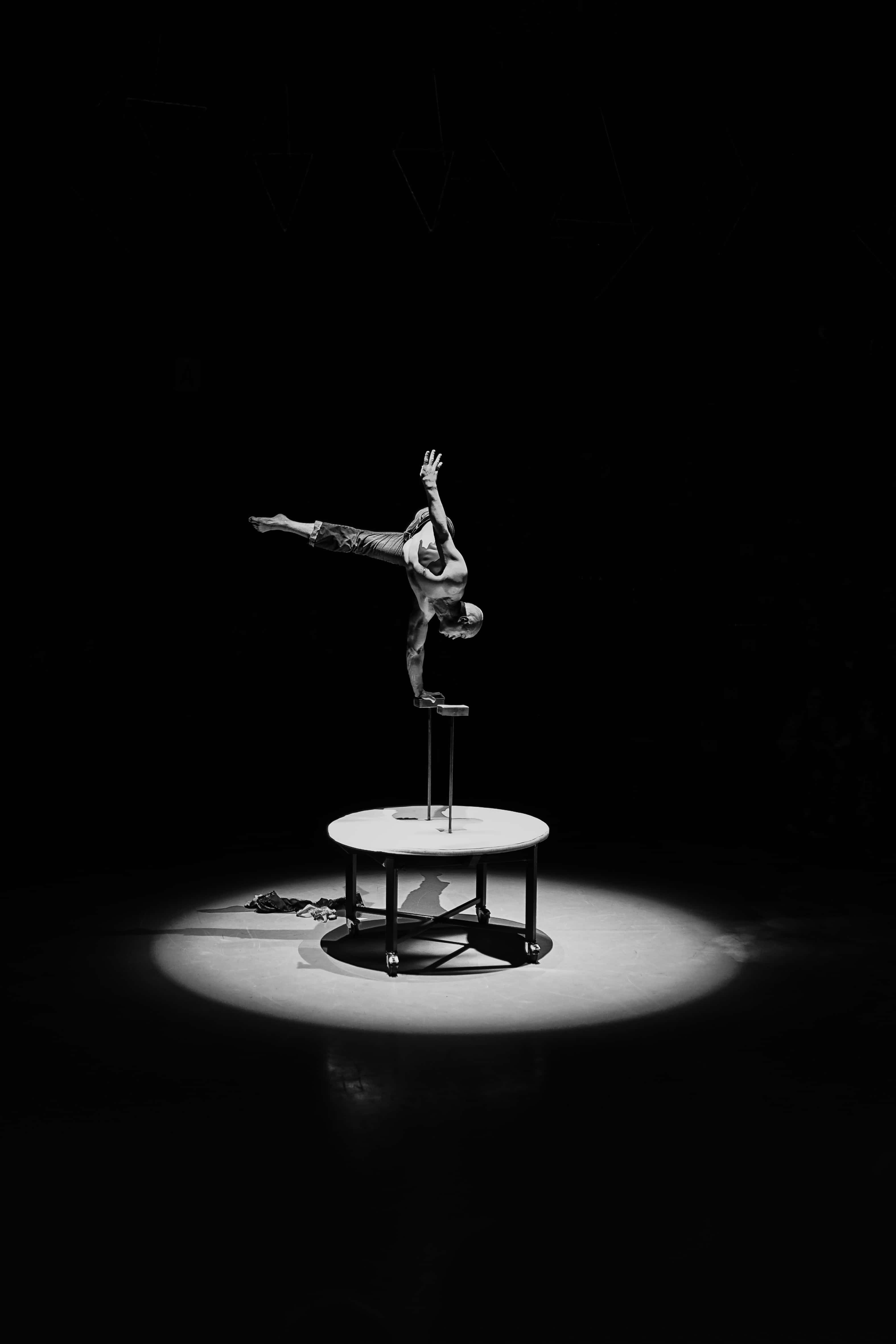 Circus 桌布 壁紙 — 一位柔術表演者在黑暗工作室的聚光燈下，在一張小桌子上做出違反重力的姿勢。