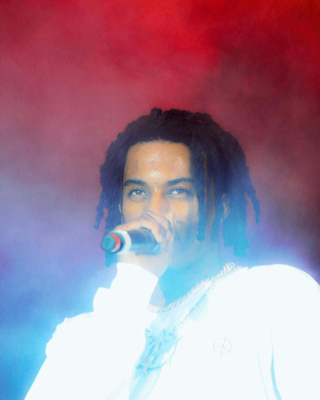 playboi carti pfp 桌布 壁紙 — 一位梳著辮子的表演者在紅色和藍色舞台燈光下，煙霧繚繞中對著麥克風唱歌。