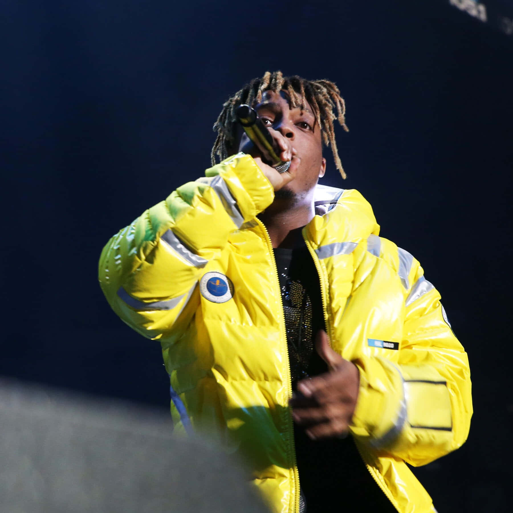 穿著黃色羽絨外套的說唱歌手拿著麥克風在舞台上表演。 — Juice Wrld 壁紙