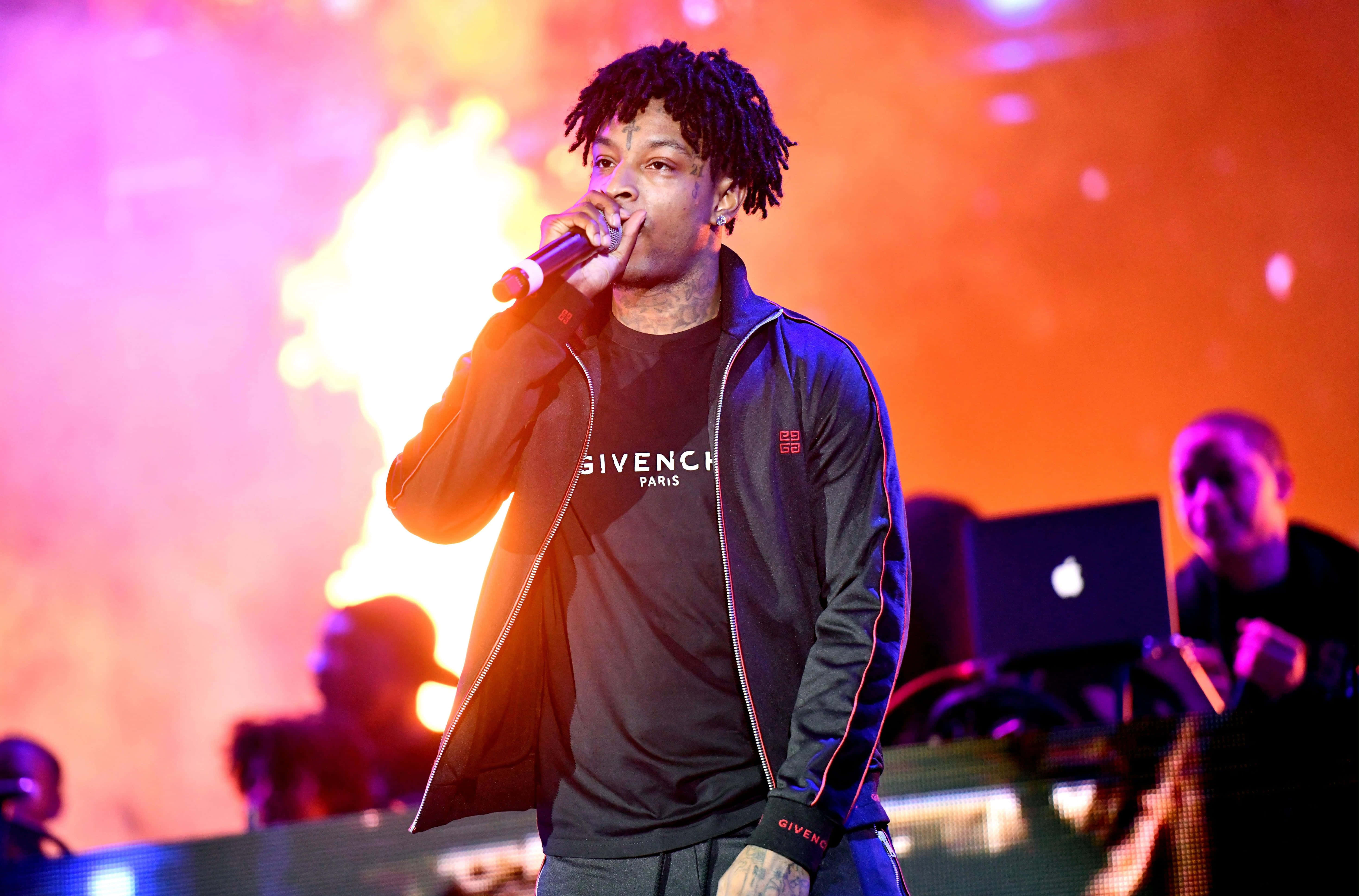 21 Savage 桌布 壁紙 — 一位梳著辮子的說唱歌手在熾熱的橙色和粉紅色燈光下拿著麥克風在舞台上表演。
