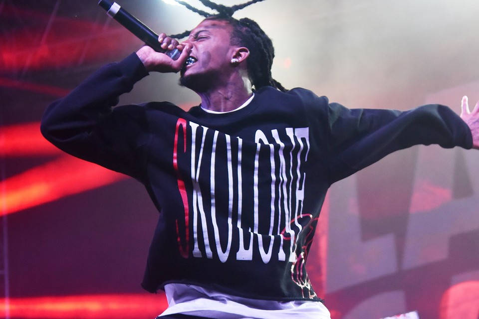 Carti 桌布 壁紙 — 一位梳著辮子的說唱歌手在紅燈下熱情地拿著麥克風在舞台上表演。