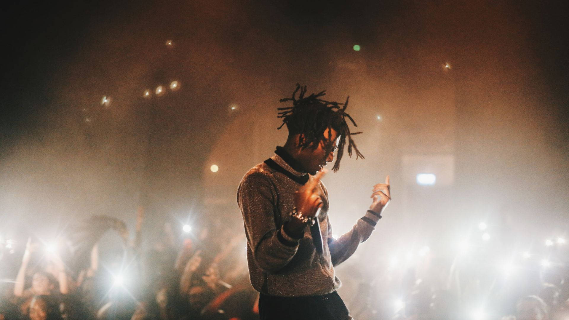 Carti 桌布 壁紙 — 一位梳著辮子的音樂家在煙霧瀰漫的舞台上表演，沐浴在溫暖的燈光中，粉絲們舉起發光的手機。