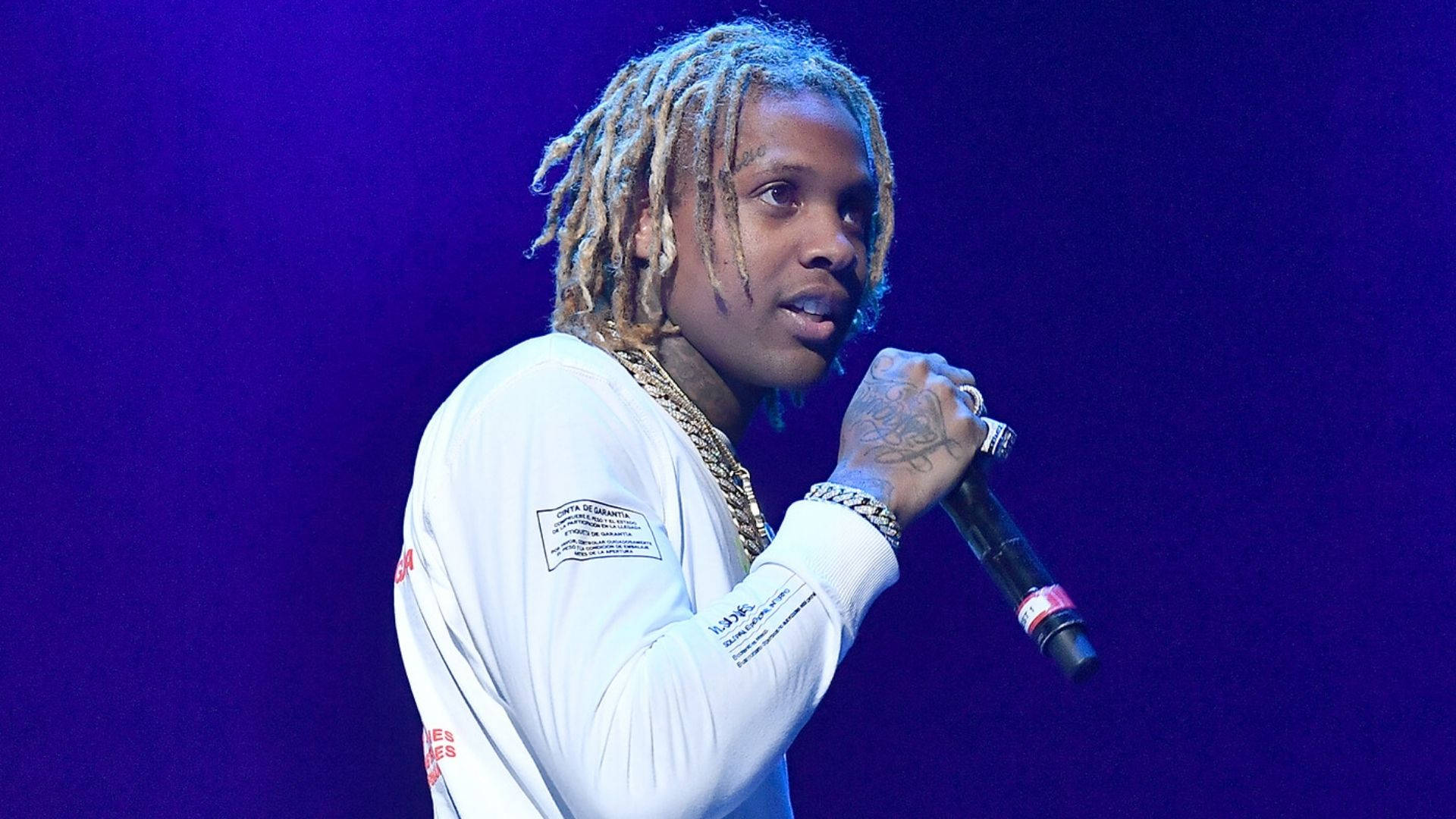 Lil Durk 桌布 壁紙 — 一位梳著辮子的饒舌歌手在紫色燈光下拿著麥克風在舞台上表演。