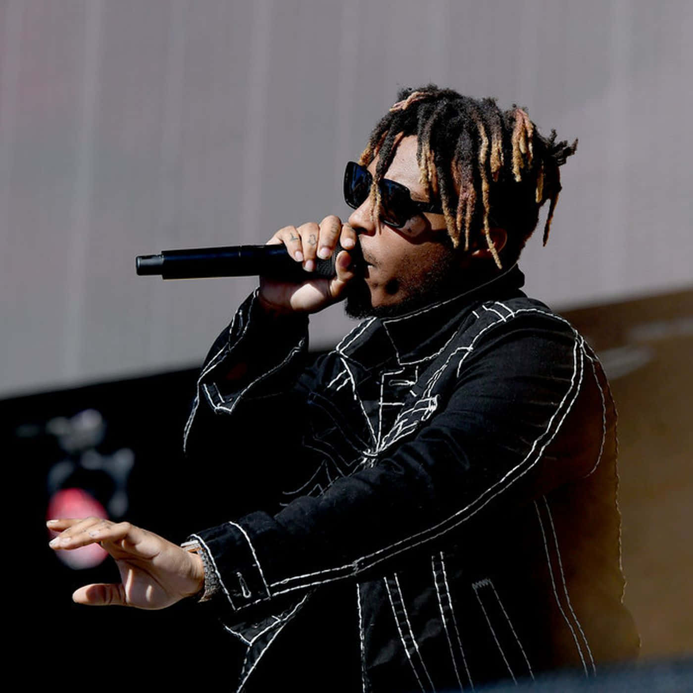 Dead Rappers 桌布 壁紙 — 一位梳著辮子頭、戴著太陽眼鏡的饒舌歌手，在明亮的日光下於舞台上對著麥克風熱情表演。