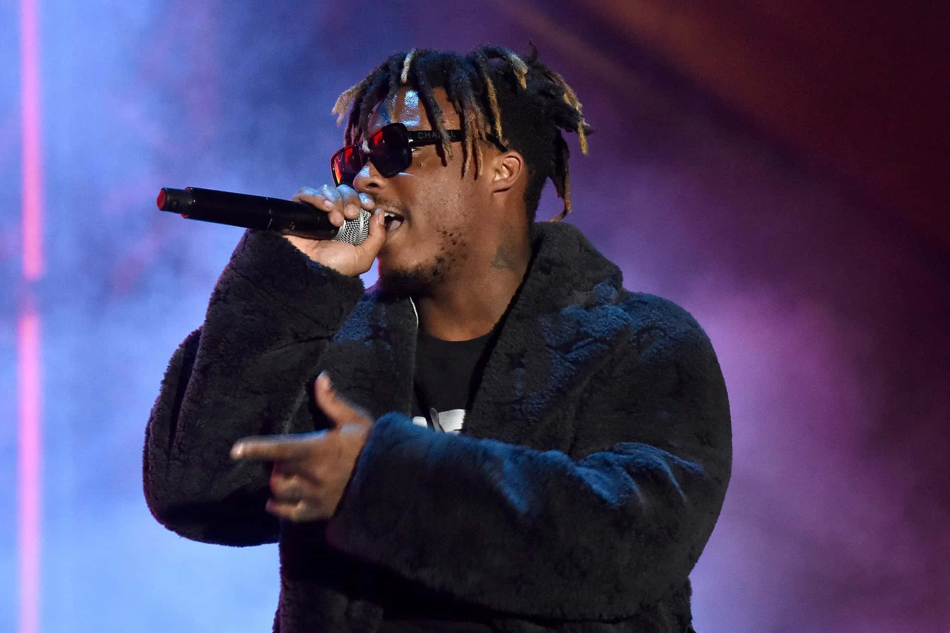 饒舌歌手在彩色燈光下戴著太陽眼鏡和麥克風在舞台上表演。 — Juice Wrld 壁紙