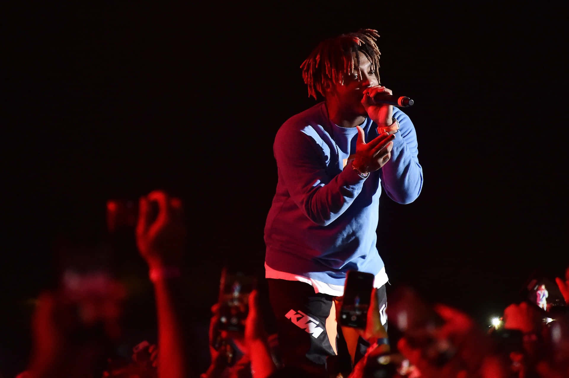 饒舌歌手在夜間演唱會上表演，紅色燈光，人群舉著手機。 — Juice Wrld 壁紙