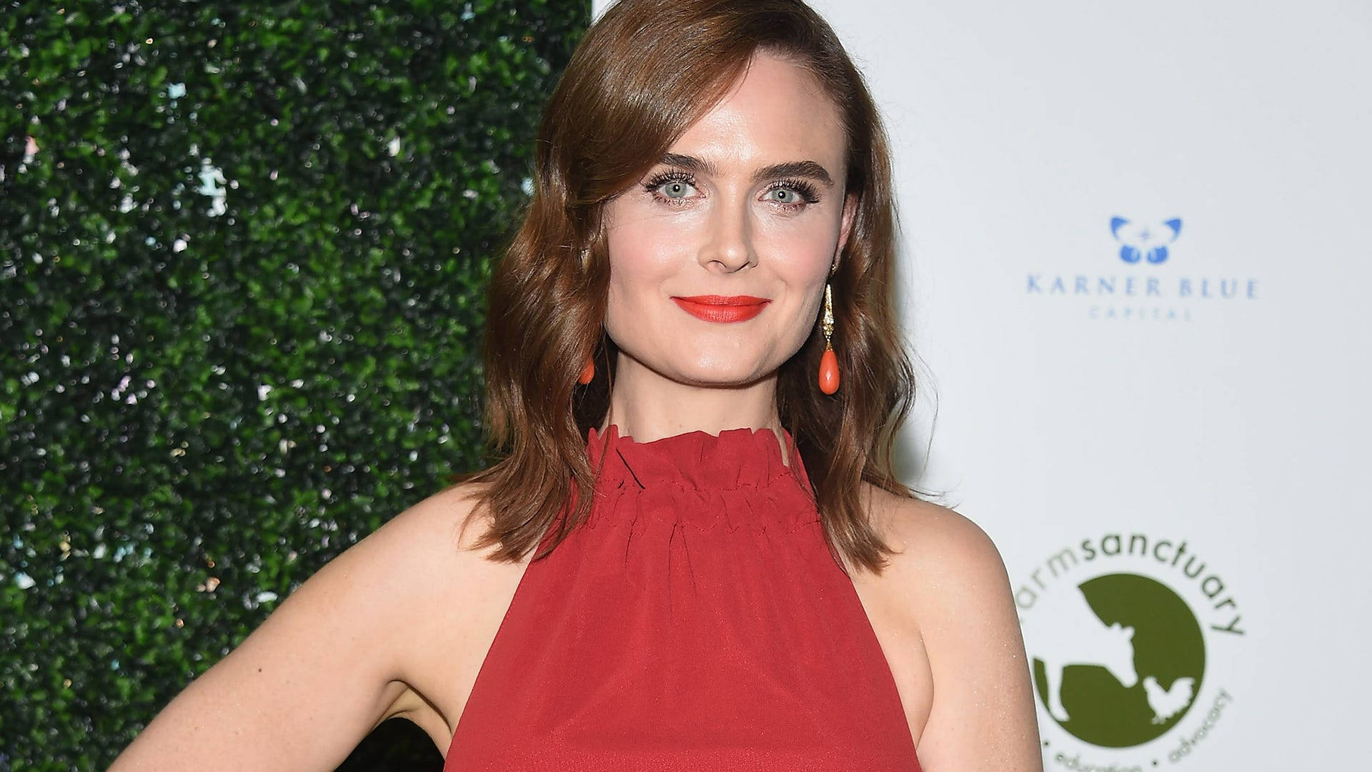 Celebrity 桌布 壁紙 — 一位棕色頭髮、塗著紅色口紅的女性，穿著紅色掛脖連衣裙，在綠色樹籬和白色活動背景前微笑。