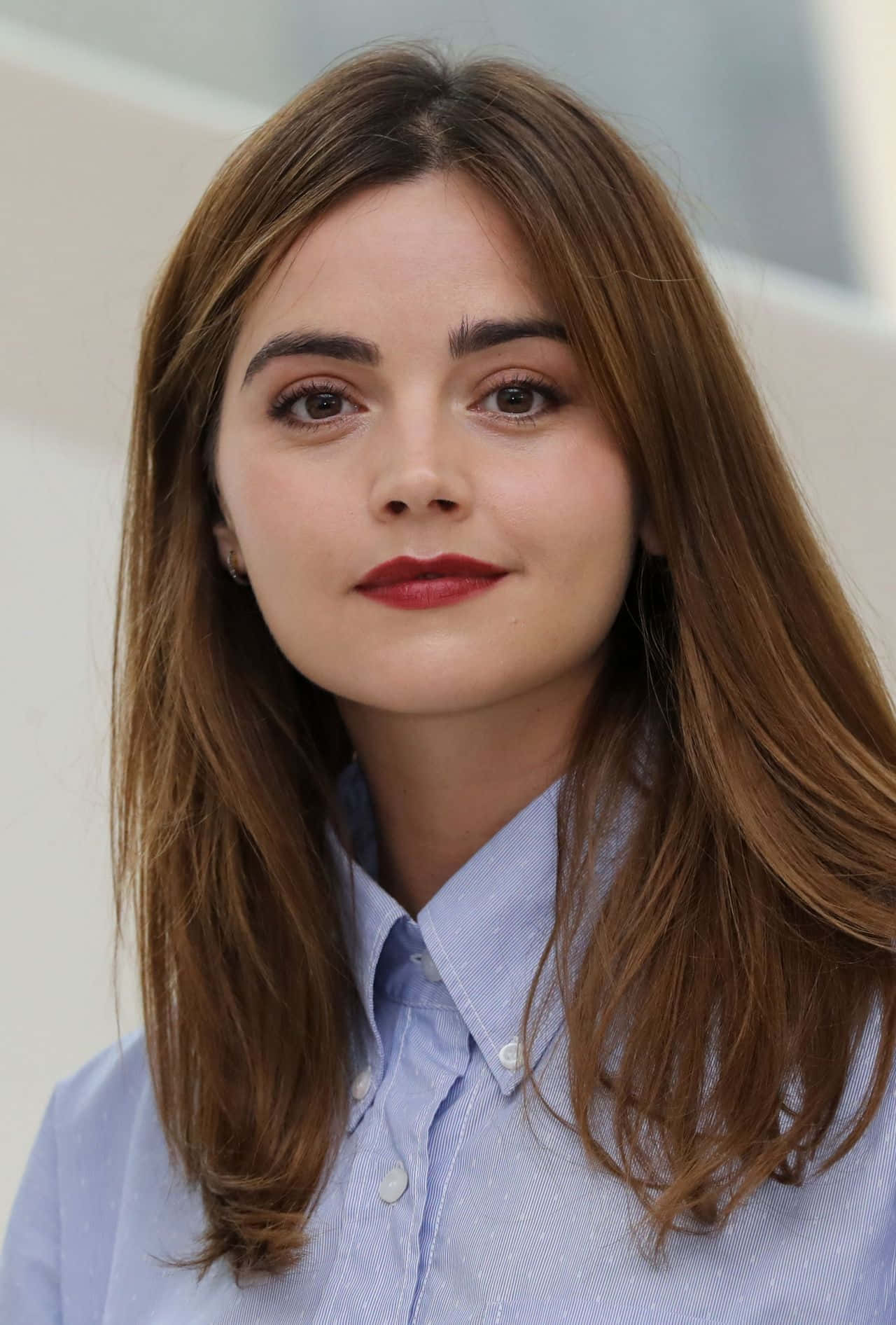 Jenna Coleman 桌布 壁紙 — 一位棕色頭髮、塗著紅色唇膏的女性穿著淺藍色鈕扣襯衫的特寫肖像。