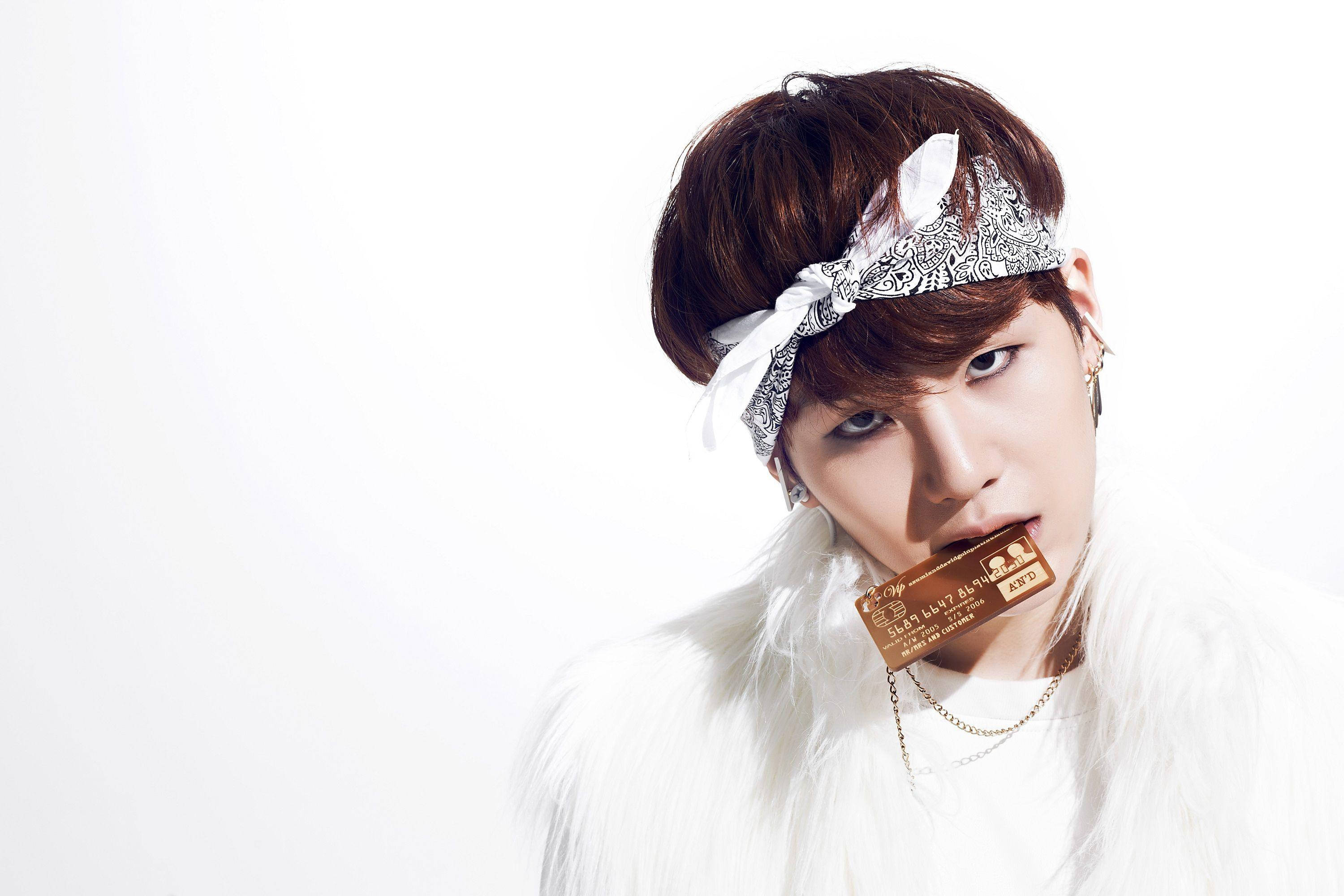 Suga Bts 桌布 壁紙 — 一位棕色頭髮、戴著圖案頭帶的年輕男子，穿著白色毛皮大衣，在純白背景前咬著一張金色信用卡。