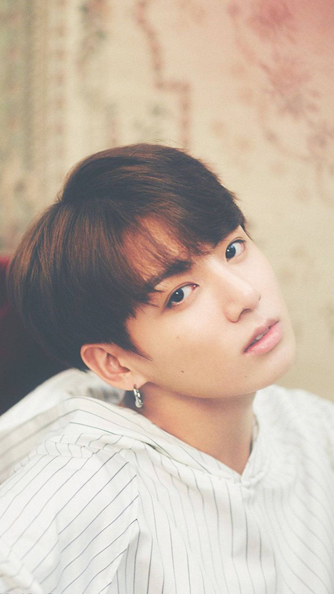 BTS 桌布 壁紙 — 一位棕色頭髮、戴著銀色耳環的年輕男子，穿著白色細條紋襯衫，在柔和的花卉壁紙背景前向上凝視。