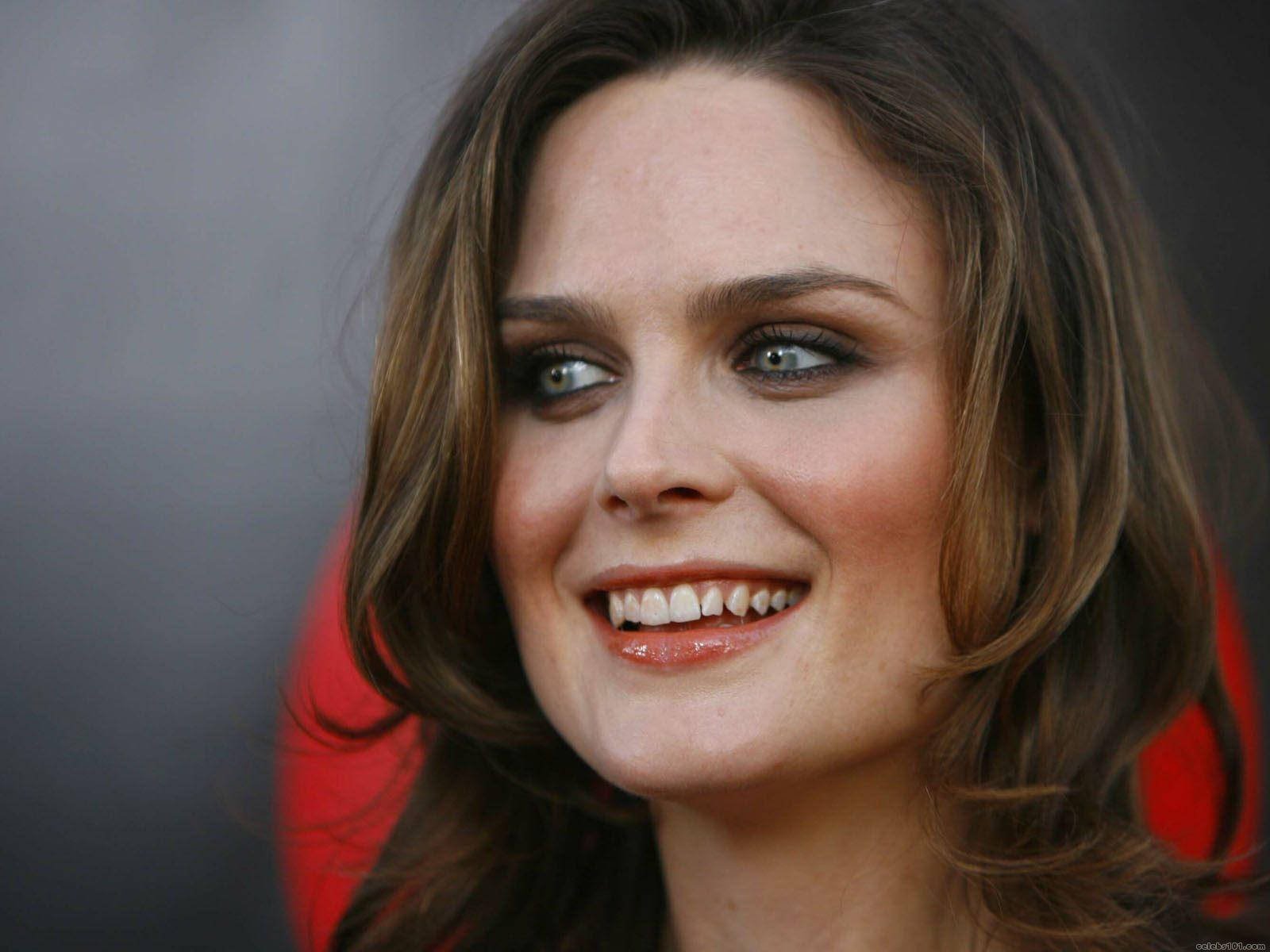 Celebrity 桌布 壁紙 — 一位棕色頭髮、明亮眼睛的女性在帶有紅色點綴的深灰色背景前溫暖微笑的特寫肖像。