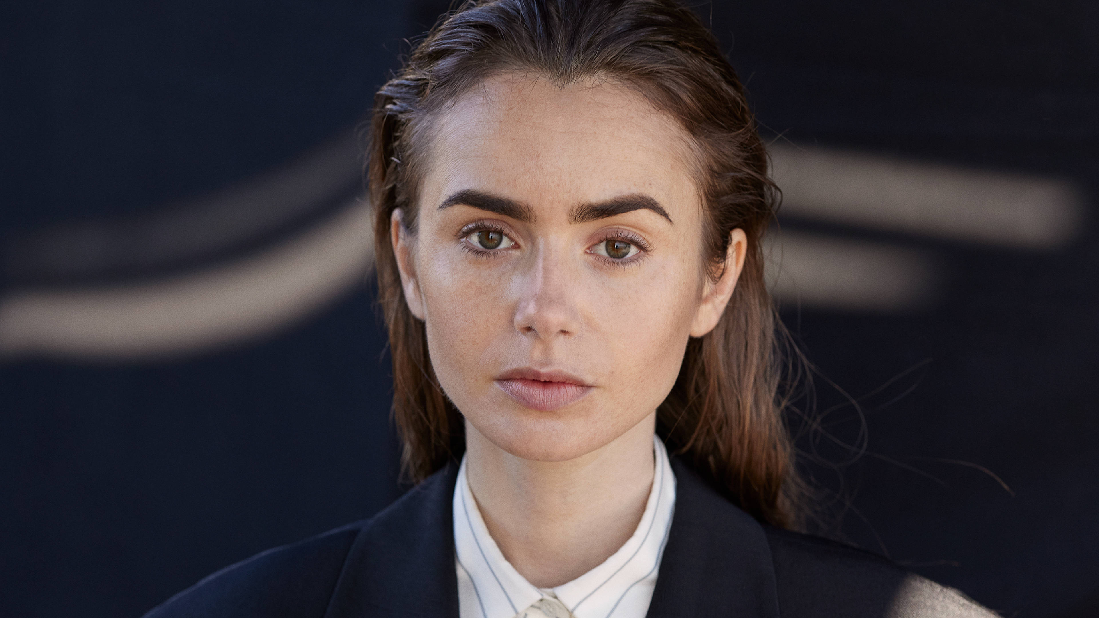 lily 桌布 壁紙 — 一位棕色頭髮、眼神強烈的女性在深色抽象背景前直視鏡頭。