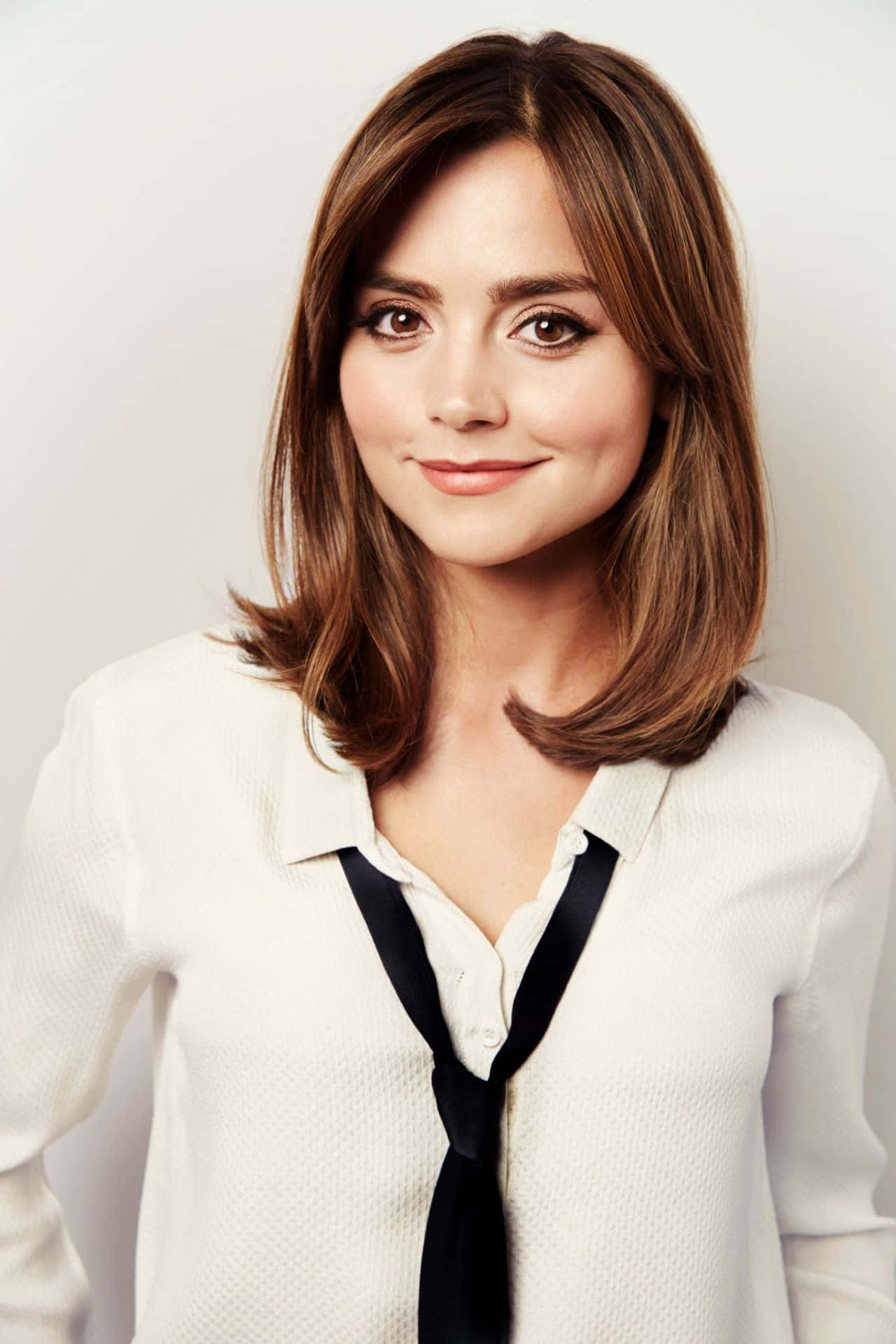 Jenna Coleman 桌布 壁紙 — 一位棕色頭髮、眼神溫暖的女性，穿著帶有黑色蝴蝶結領帶的白色質感襯衫，溫柔地微笑。