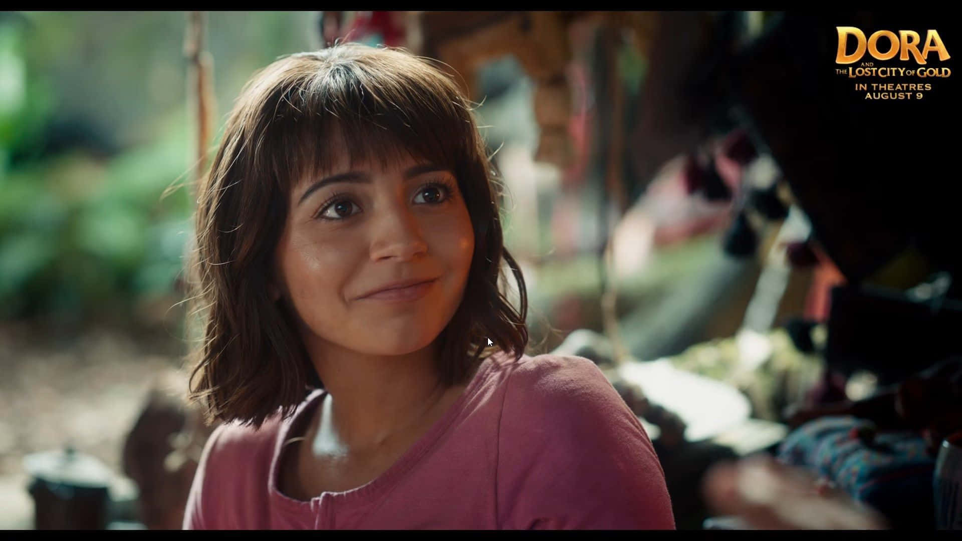 Dora 桌布 壁紙 — 一位棕色頭髮、穿著粉色襯衫的年輕女孩在陽光明媚的叢林場景中溫暖地微笑。