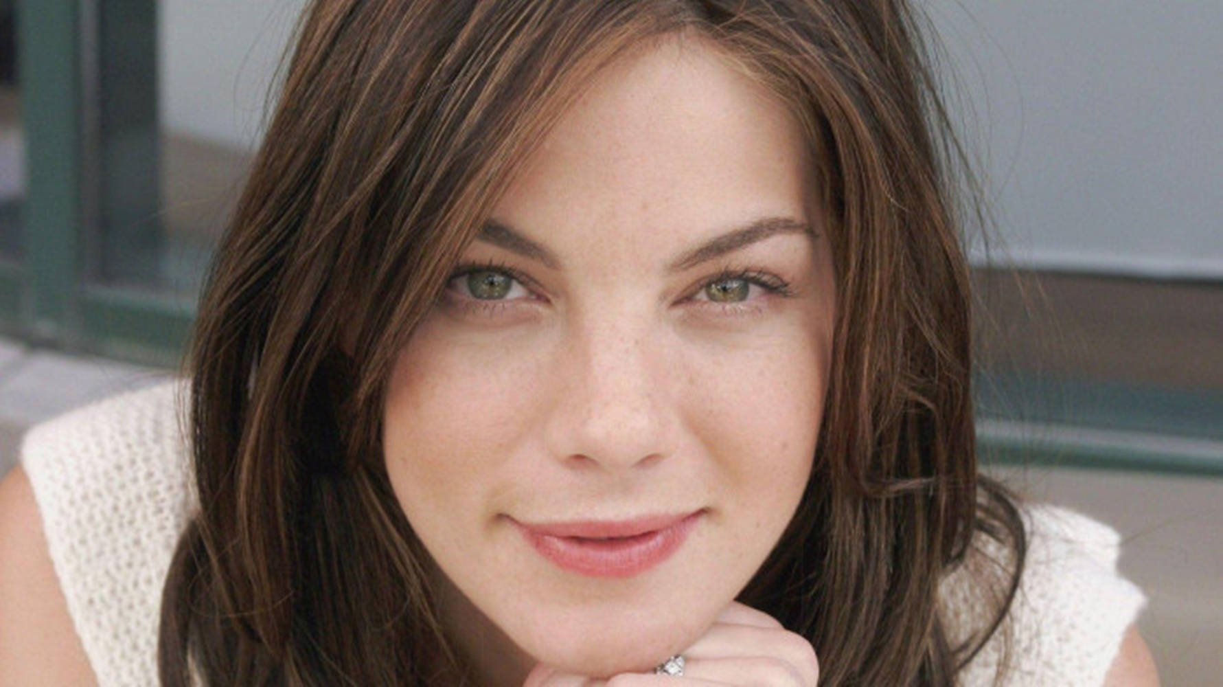 Michelle Monaghan 桌布 壁紙 — 一位棕色頭髮、綠色眼睛的女性，將下巴擱在手上，溫柔微笑的特寫肖像。