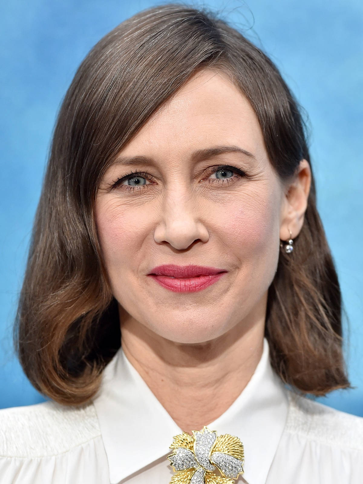 Celebrity 桌布 壁紙 — 一位棕色頭髮、綠色眼睛的女性在純藍色背景前微笑，身穿白色襯衫和華麗胸針。