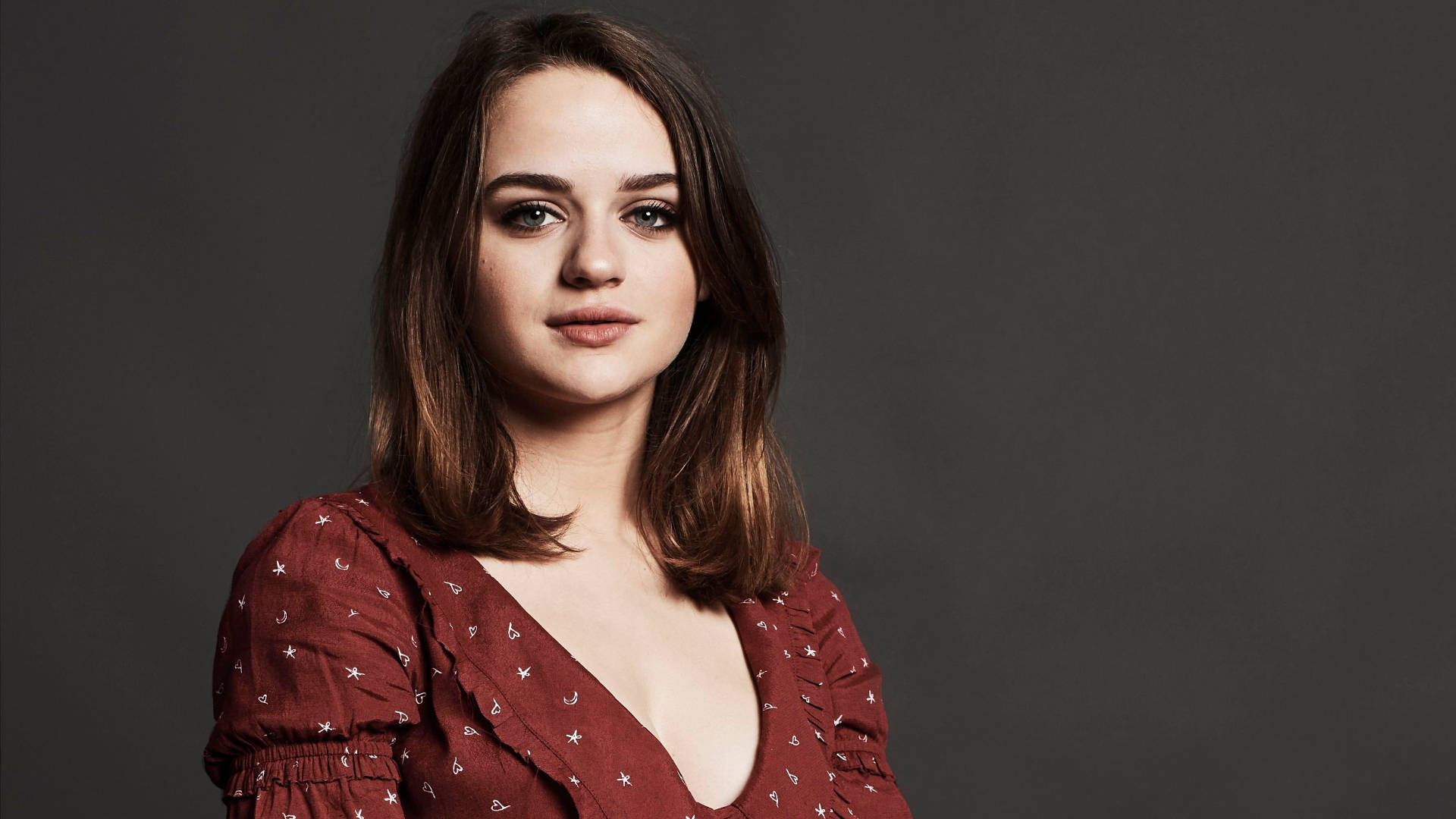 Joey King 桌布 壁紙 — 一位棕色頭髮、綠色眼睛的年輕女性穿著紅色星星圖案的上衣，背景是深灰色的攝影棚。