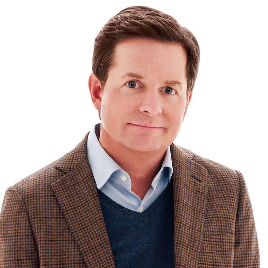 michael j fox 桌布 壁紙 — 一位棕色頭髮、藍色眼睛的男人，在白色背景前，身穿棕色格子西裝外套，內搭藍色毛衣和淺藍色襯衫。