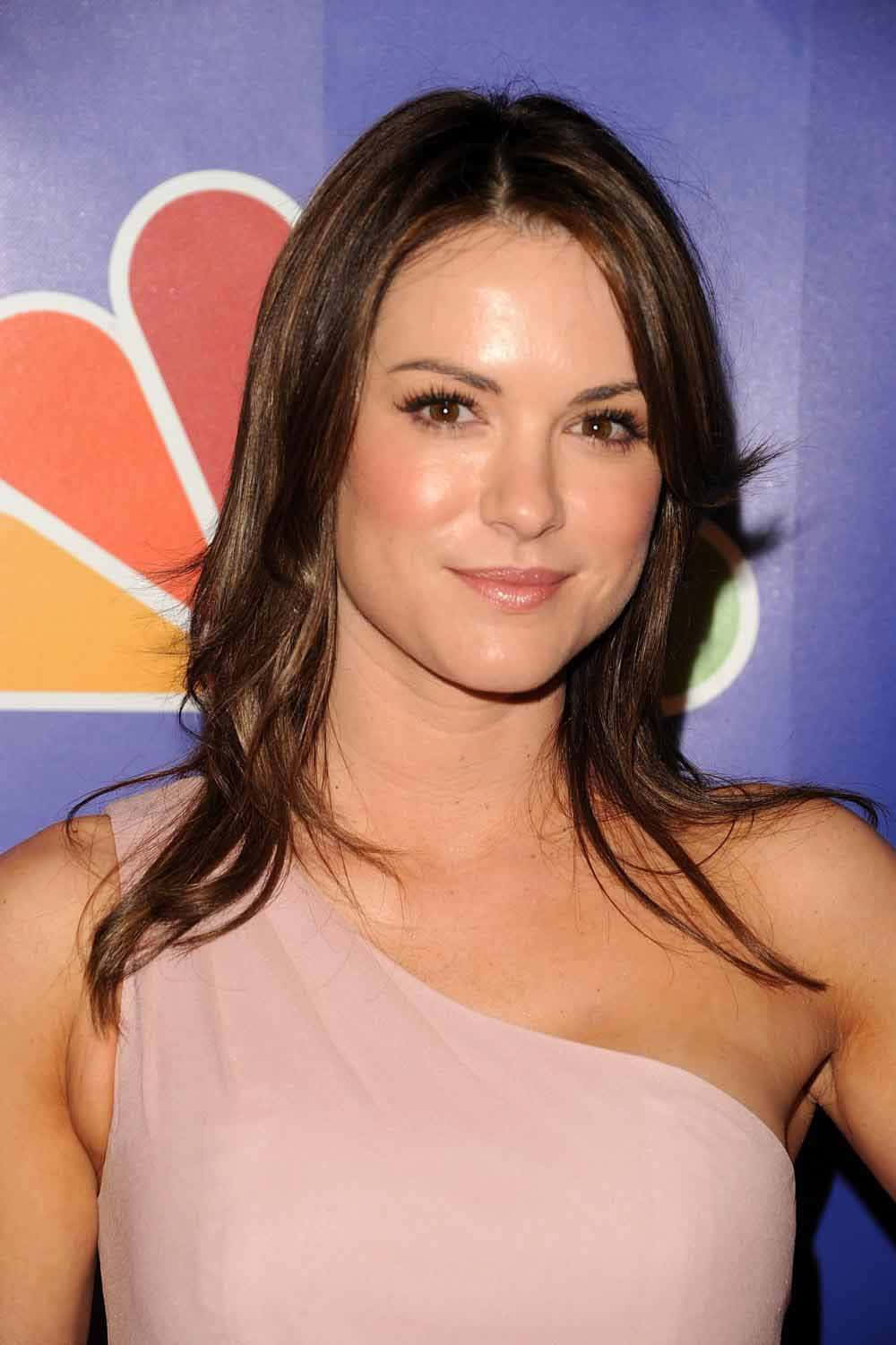 Danneel Ackles 桌布 壁紙 — 一位棕色頭髮、身穿粉紅色連衣裙的女性在藍色NBC標誌背景前對著鏡頭微笑。
