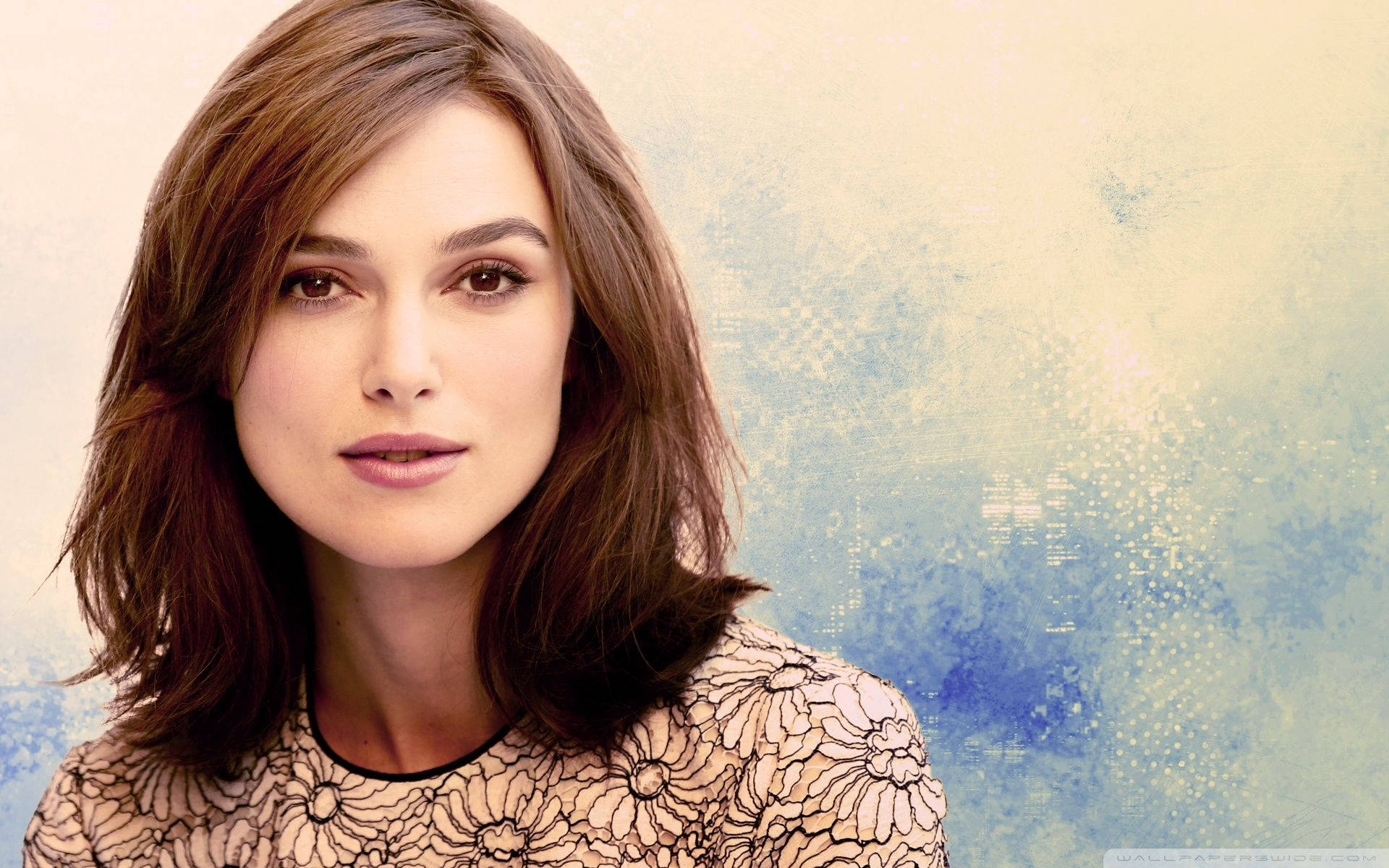 Keira Knightley 桌布 壁紙 — 一位棕色頭髮、身穿花卉上衣的女性，在柔和的藍色和米色紋理背景前平靜地凝視。