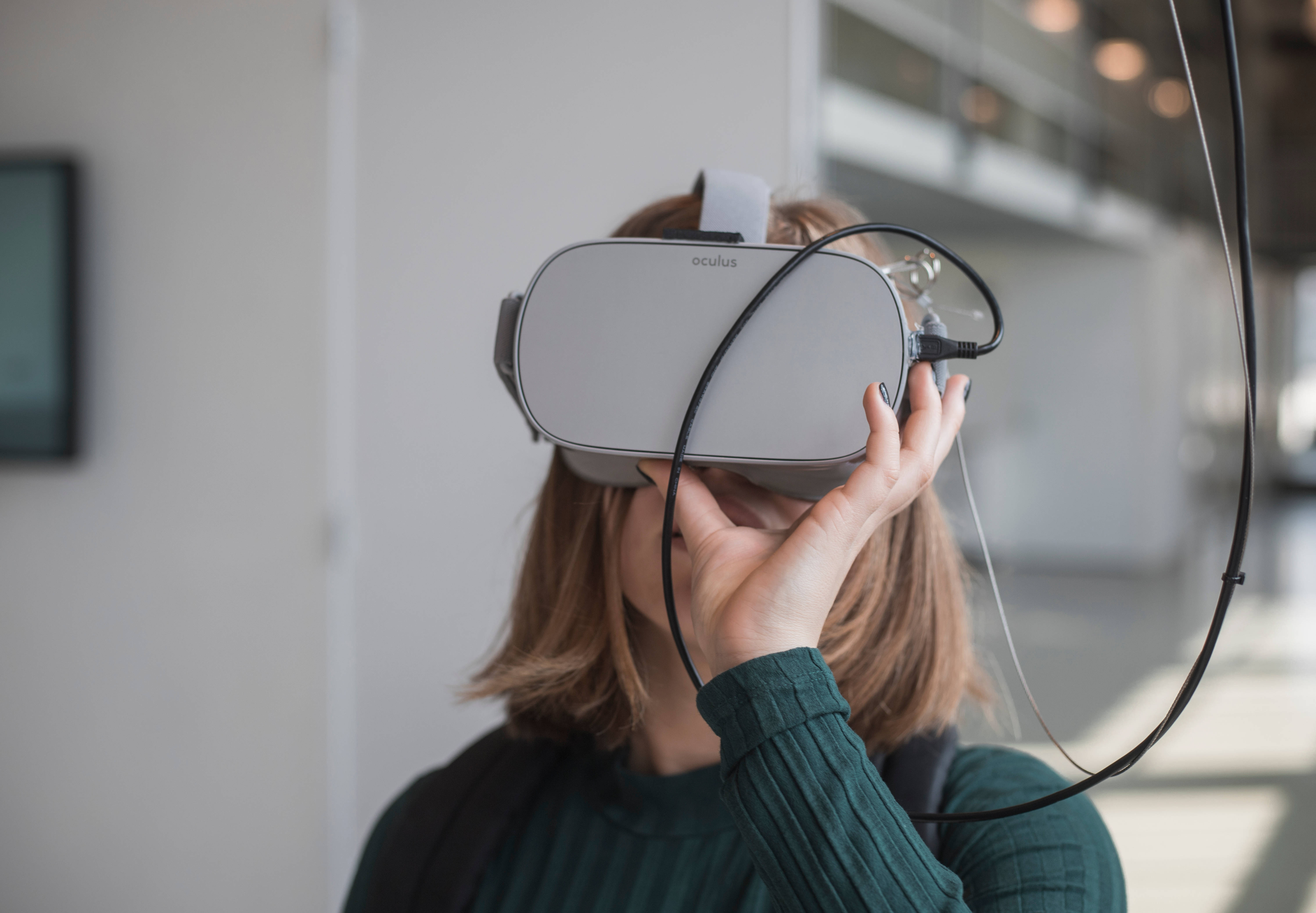 教育 桌布 壁紙 — 一位棕色頭髮的人士在現代室內空間中調整灰色Oculus VR頭戴式裝置。