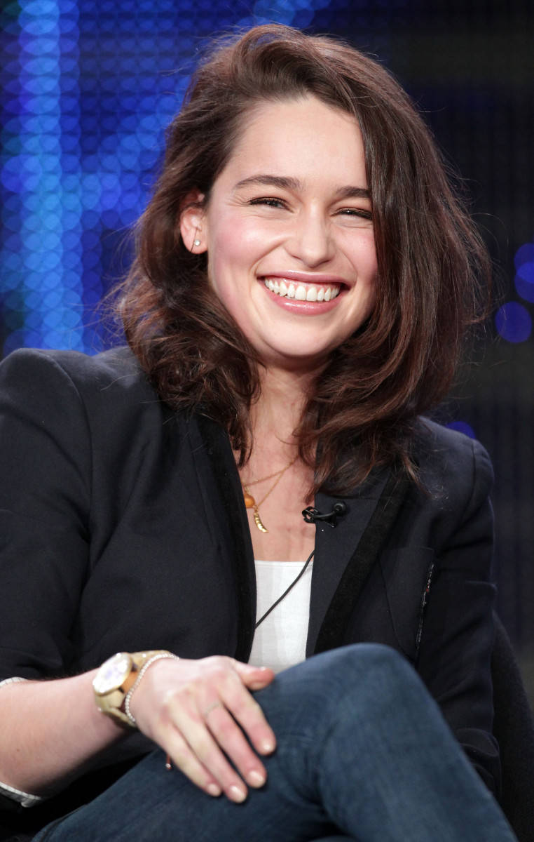Emilia 桌布 壁紙 — 一位棕色頭髮的女性坐在藍色六邊形圖案背景前，露出燦爛的笑容。